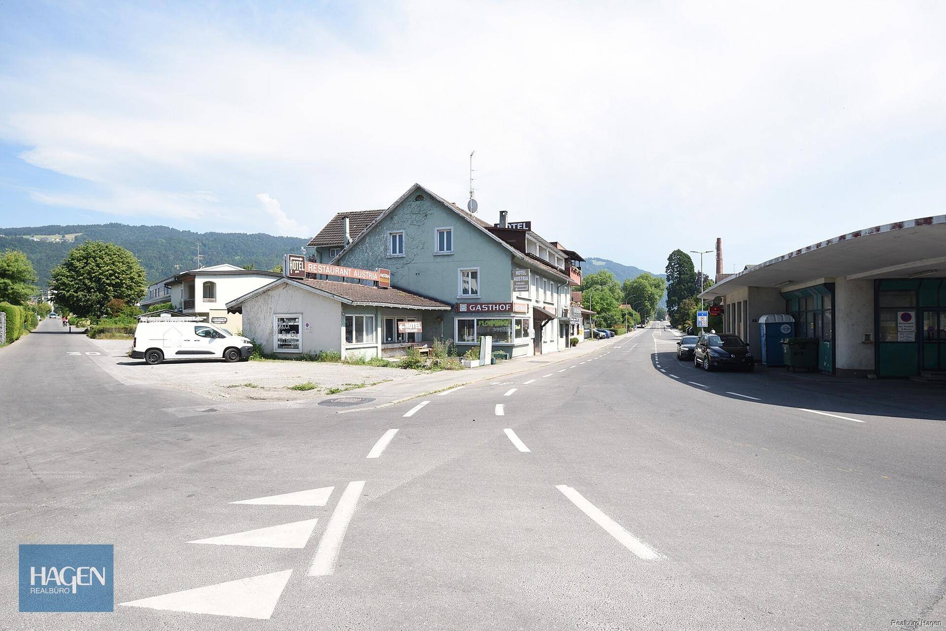 Blick auf eine Straße mit einem Gasthofgebäude und umliegenden Häusern in einer ländlichen Umgebung.