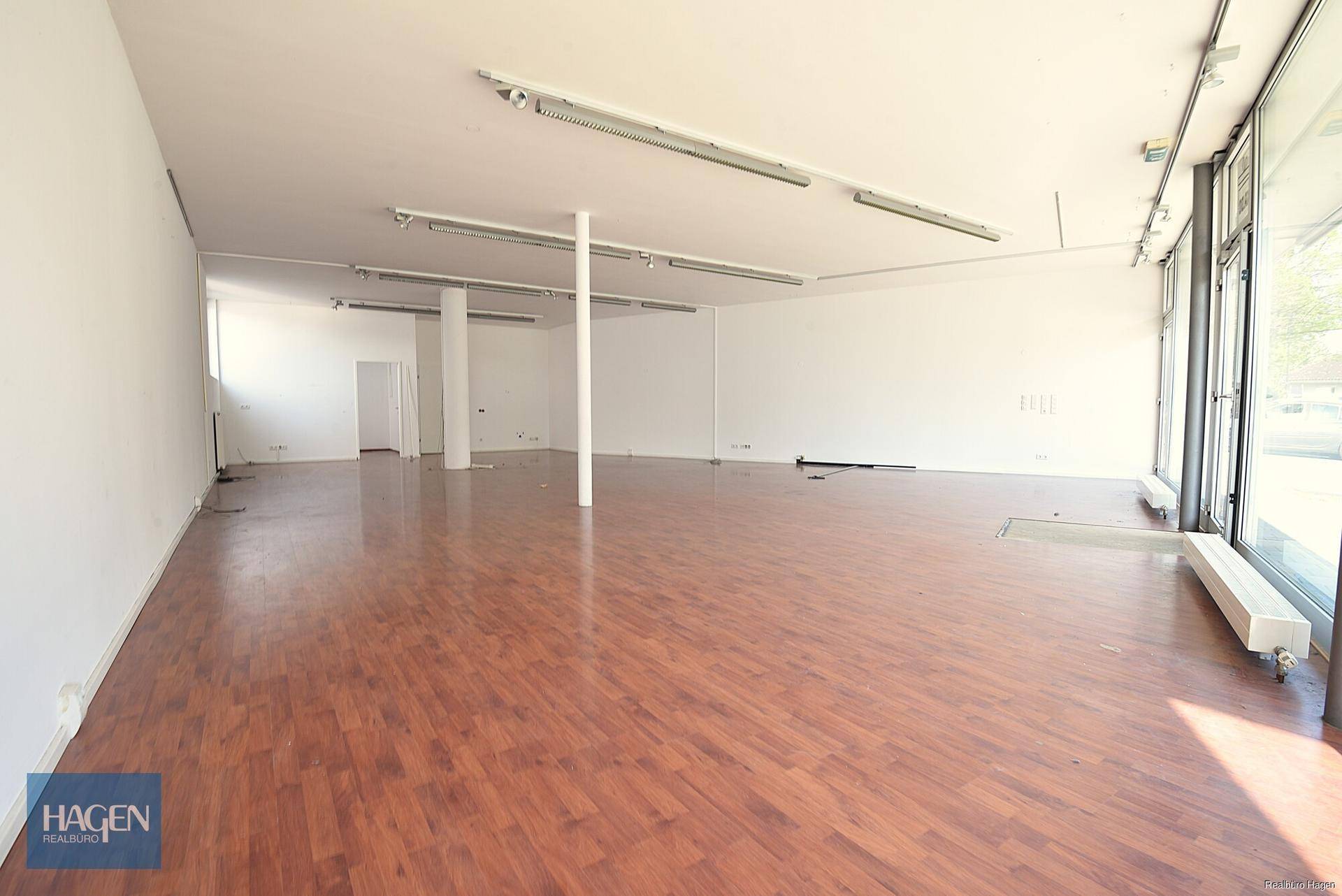 Geräumiger, leerer Gewerberaum mit Holzboden und großen Fenstern, bereit für individuelle Gestaltung.