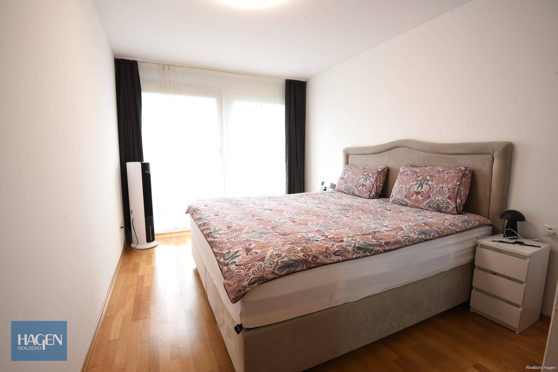 Schlafzimmer mit Doppelbett, Parkettboden und großen Fenstern für viel Tageslicht.