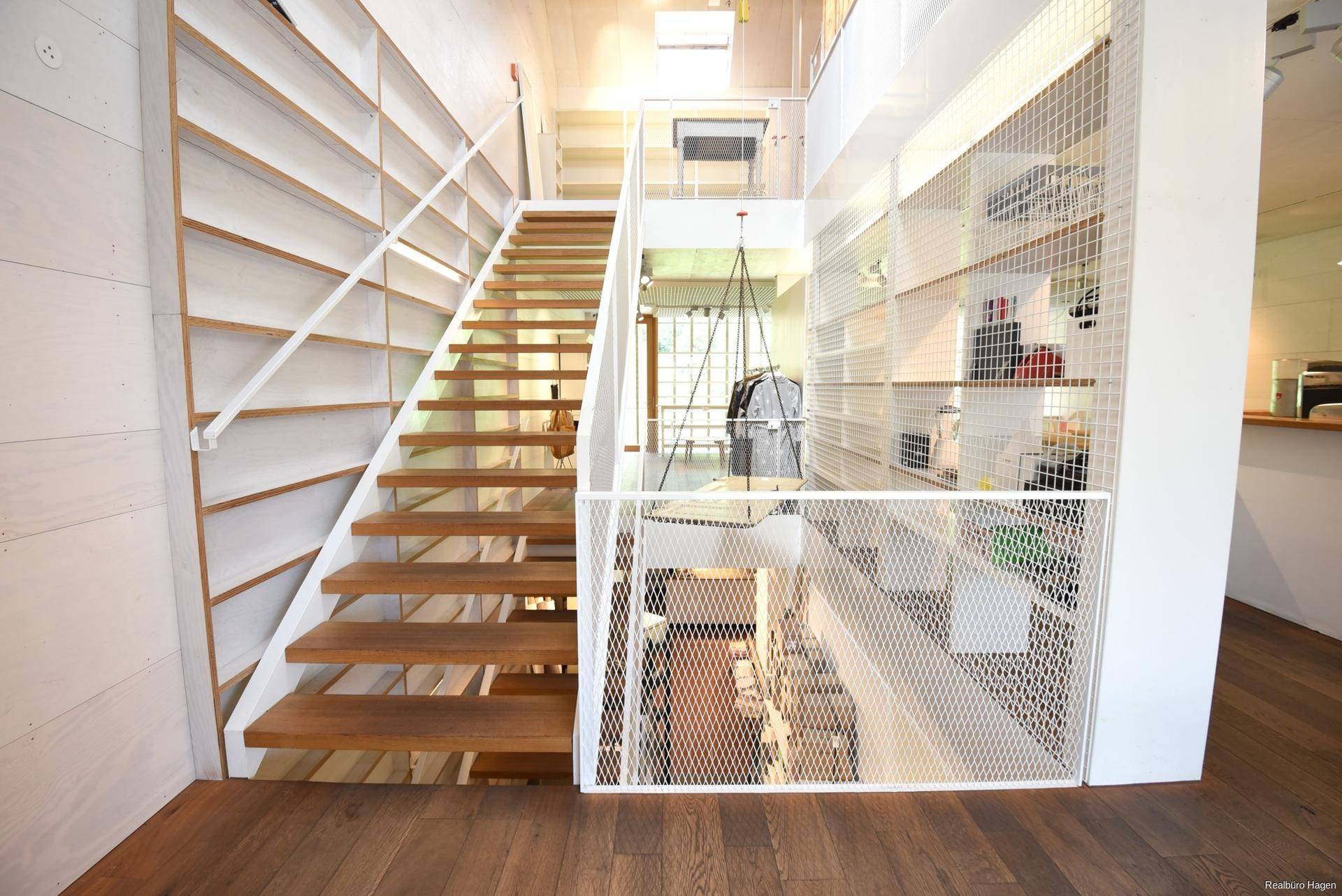 Moderne Holztreppe mit weißem Metallgeländer, die verschiedene Ebenen des offenen Raumes verbindet.