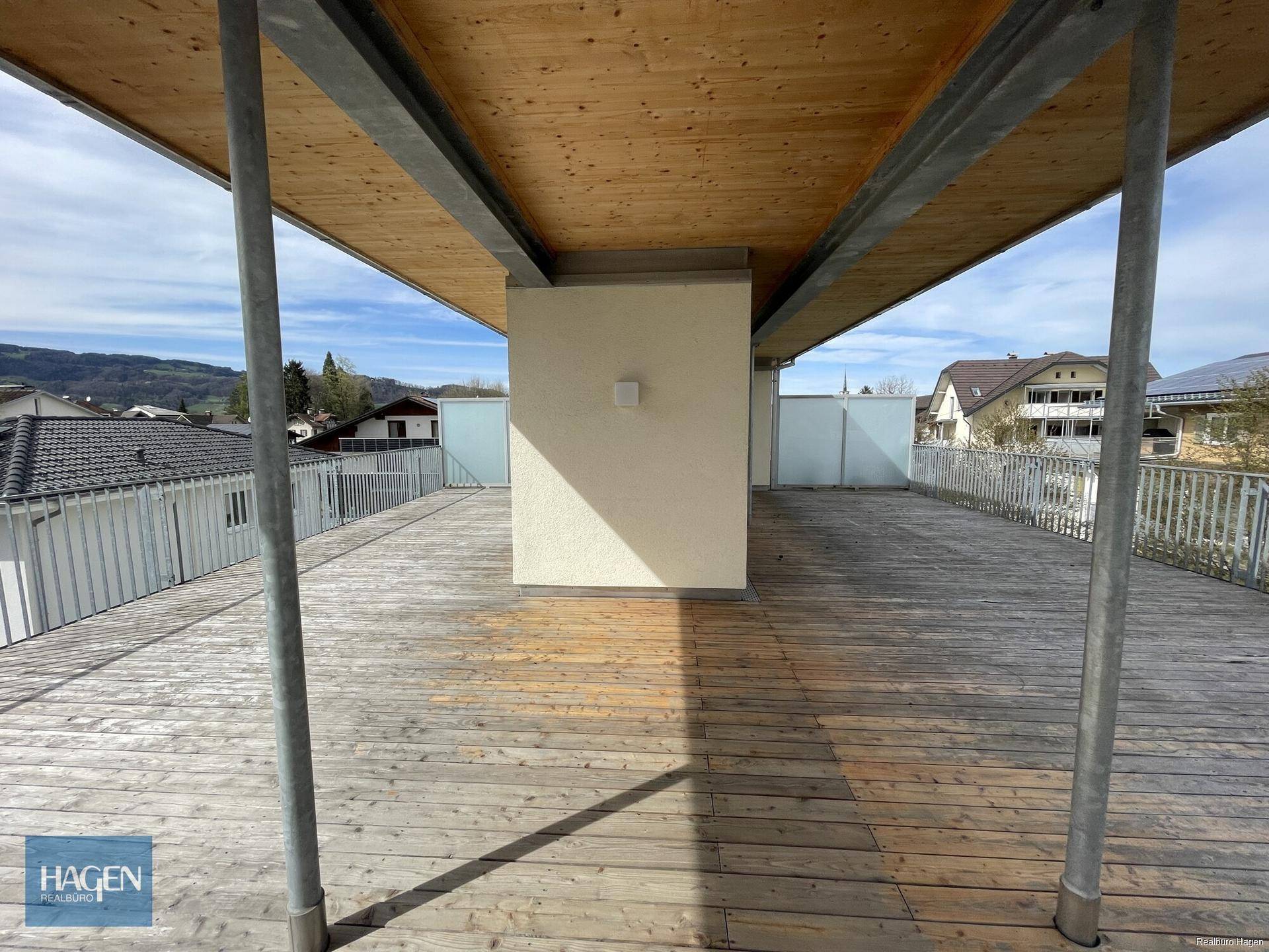 Weitläufige Holzterrasse mit Überdachung und Blick auf die umliegende Wohngegend.