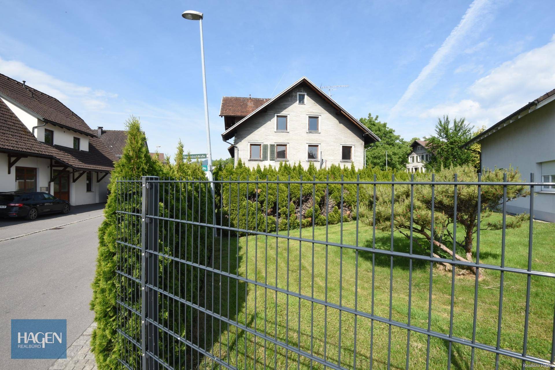 Wohnhaus mit Garten und Metallzaun, umgeben von gepflegten Hecken und Bäumen.