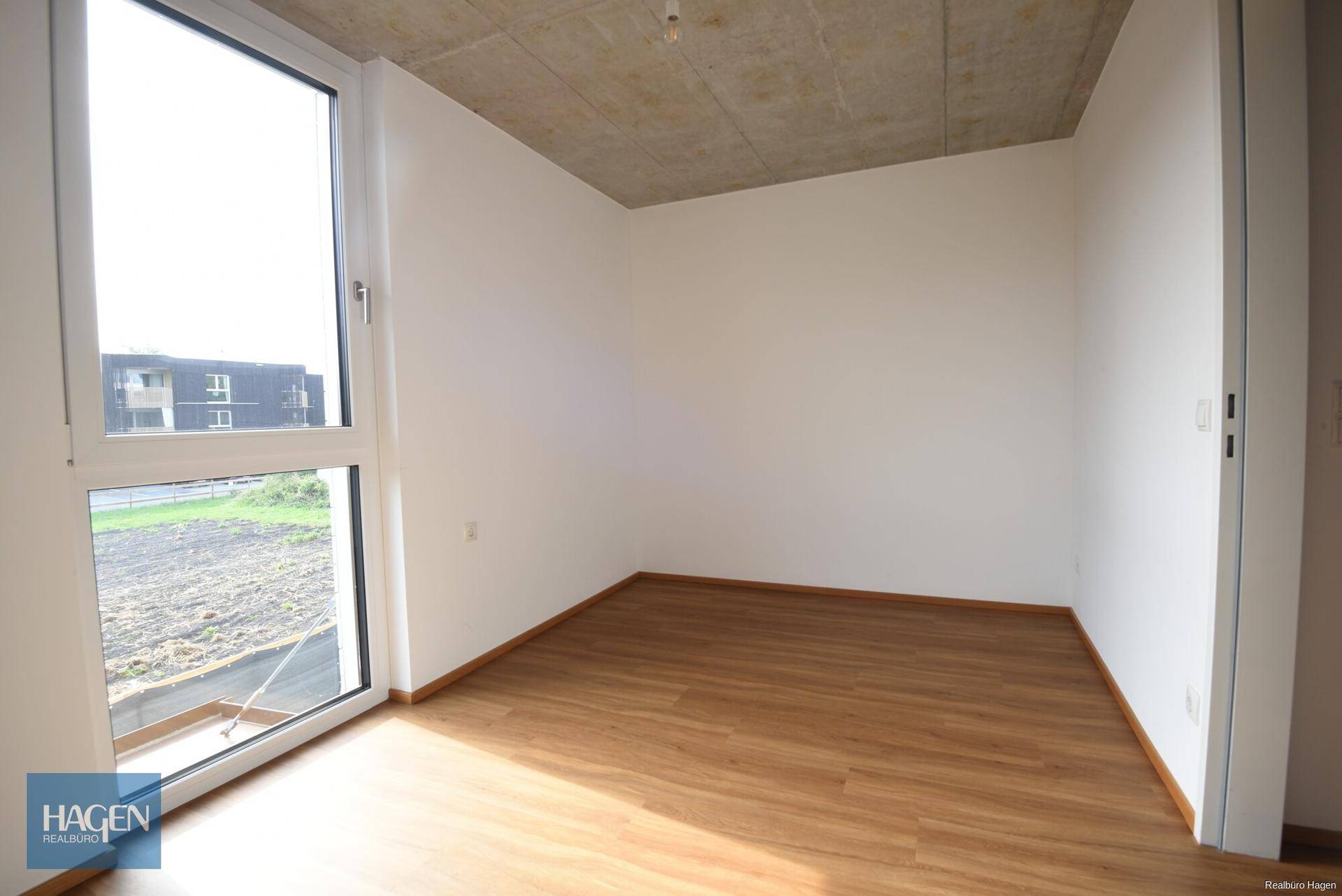 Heller Raum mit Laminatboden, hohen Decken und großem Fenster für viel Tageslicht.