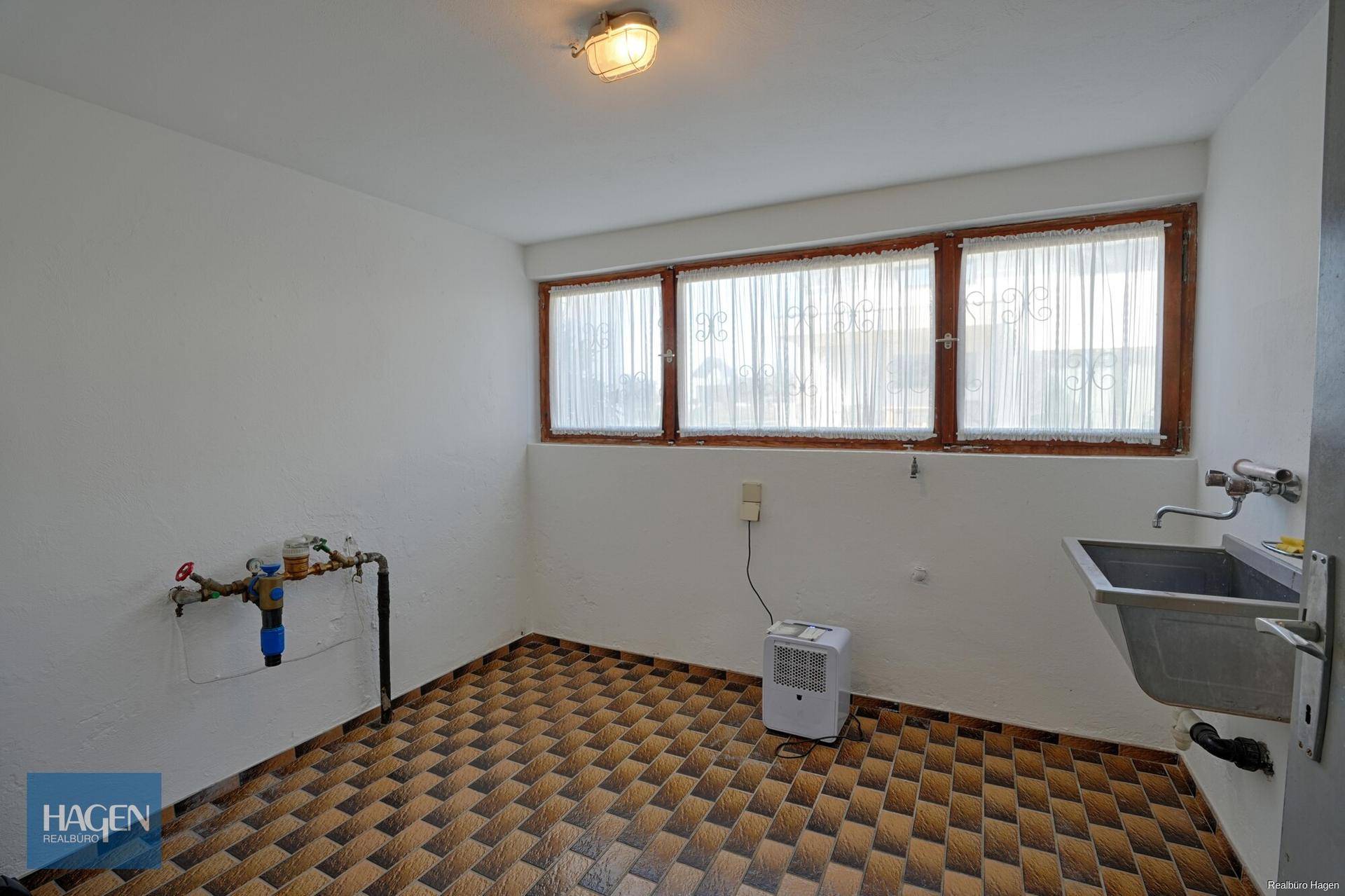 Hauswirtschaftsraum mit Waschbecken, Fenstern und funktionalem Fliesenboden.