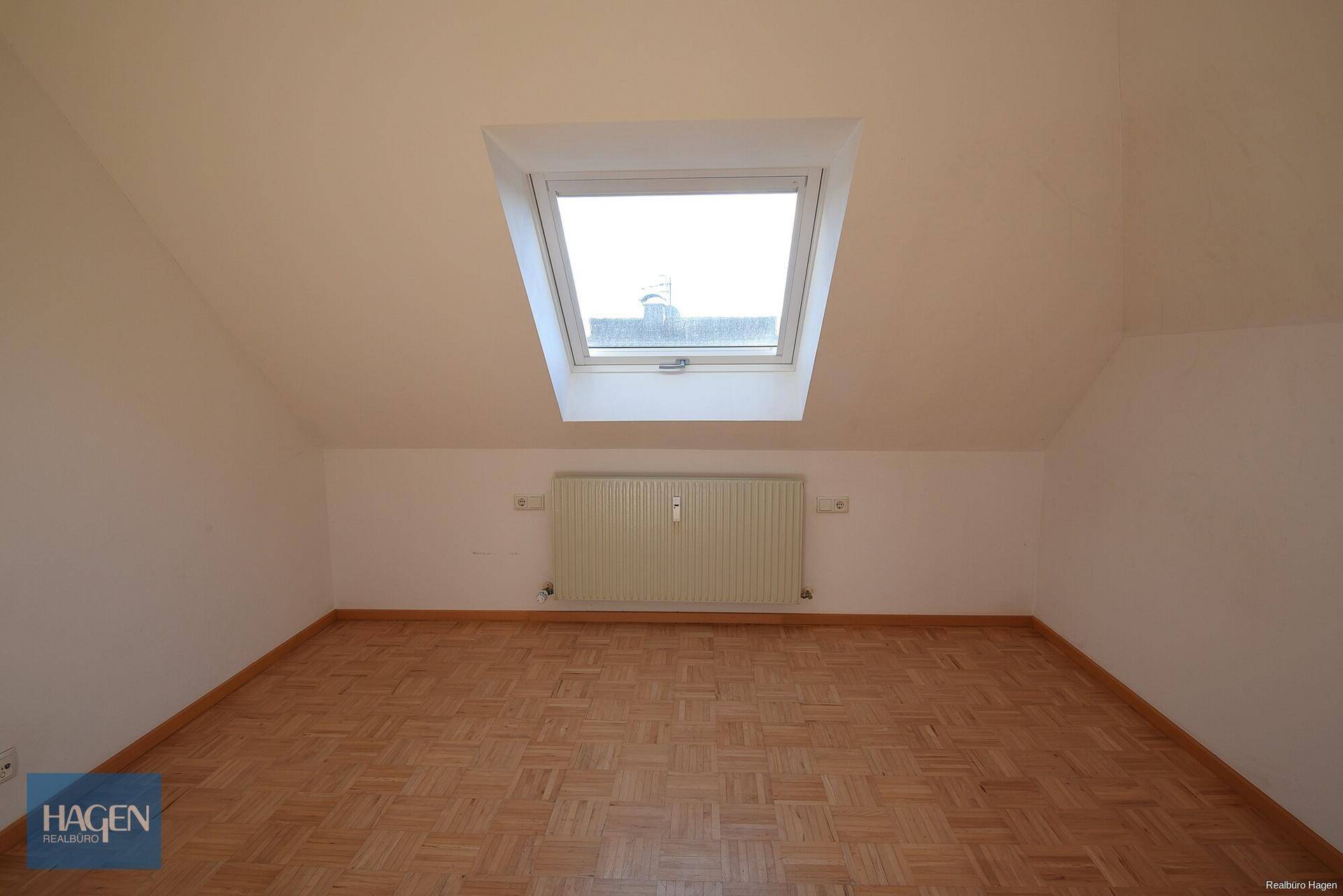 Gemütliches Schlafzimmer im Dachgeschoss mit Parkettboden, Heizkörper und großem Dachfenster.