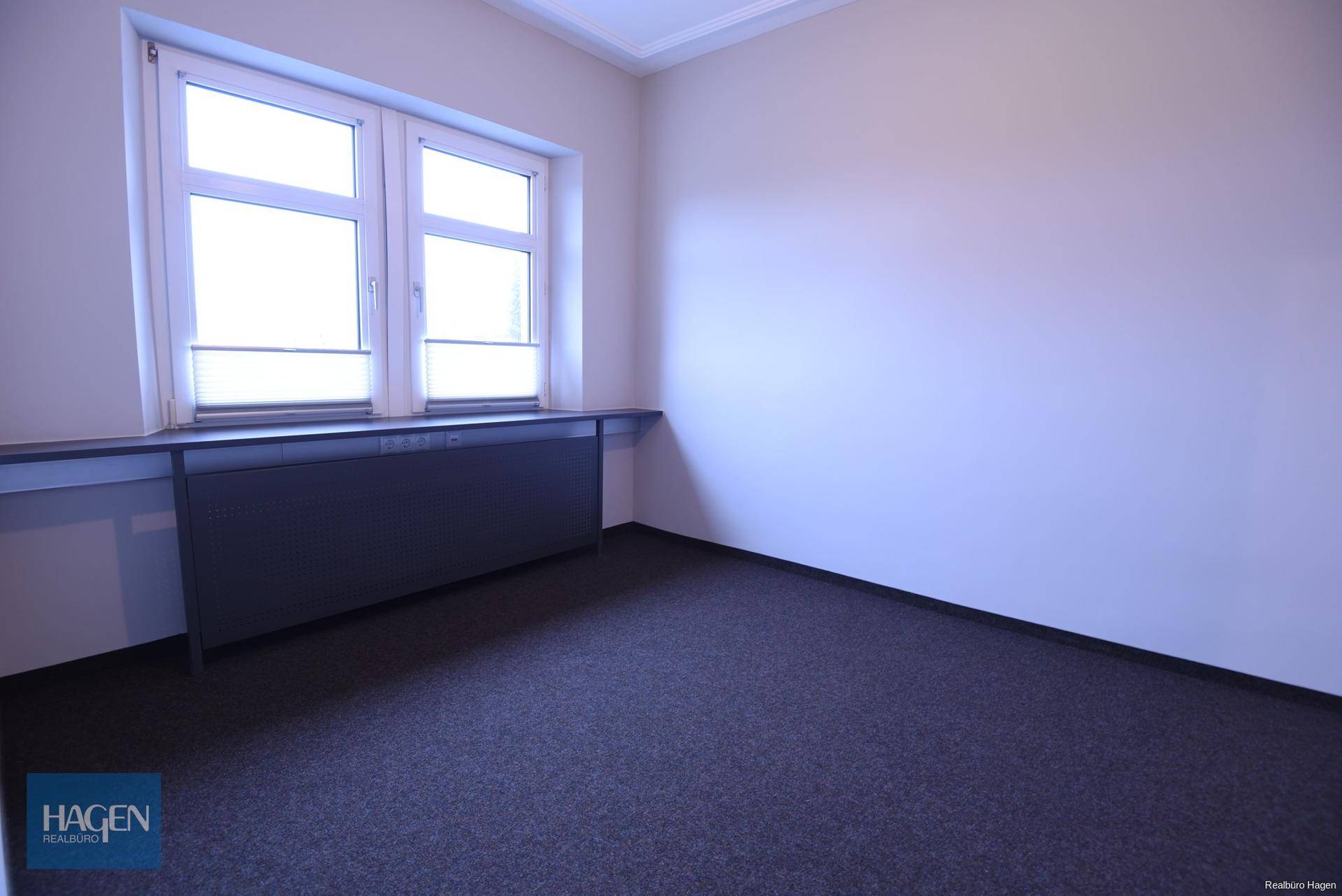 Helles Büro mit großem Fenster, das viel Tageslicht hereinlässt, und dunklem Boden.