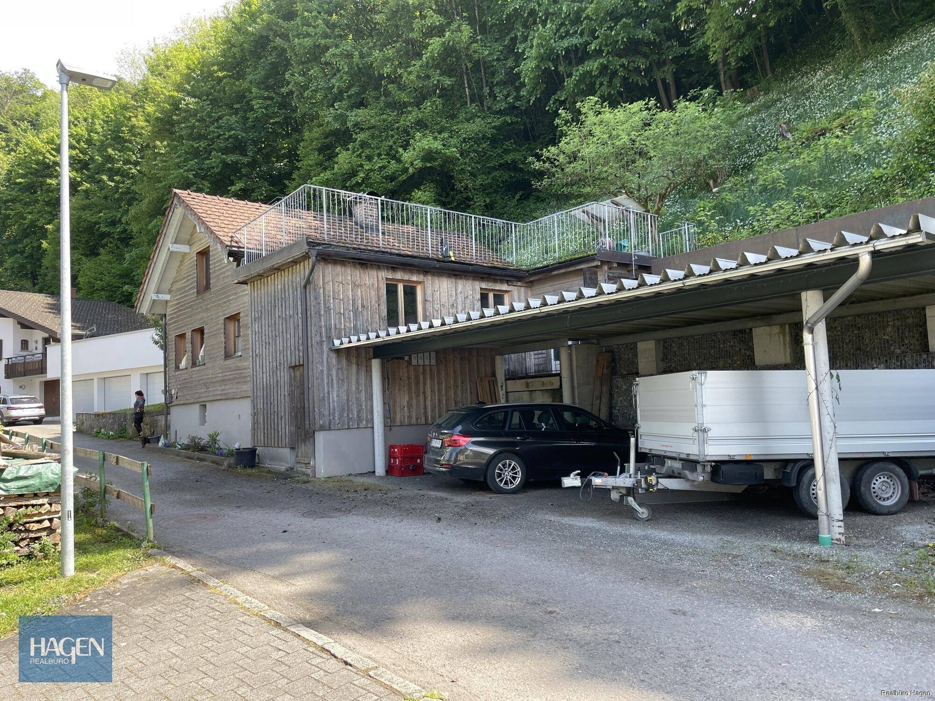 Ansicht des Holzhauses mit angrenzendem Carport und einem möglichen Dachterrassenbereich.
