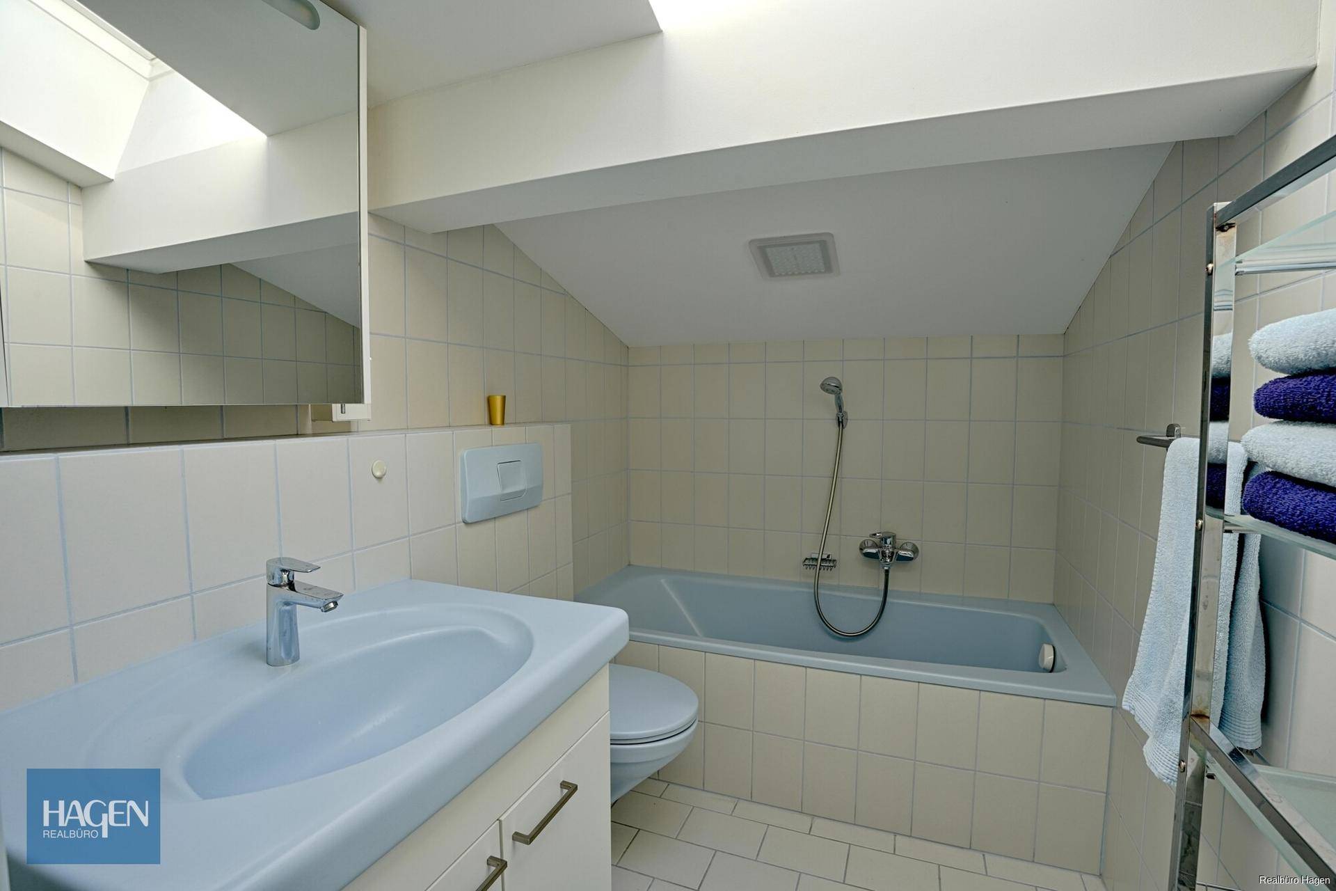 Badezimmer im Dachgeschoss mit Badewanne, Dachfenster und hellen Fliesen.