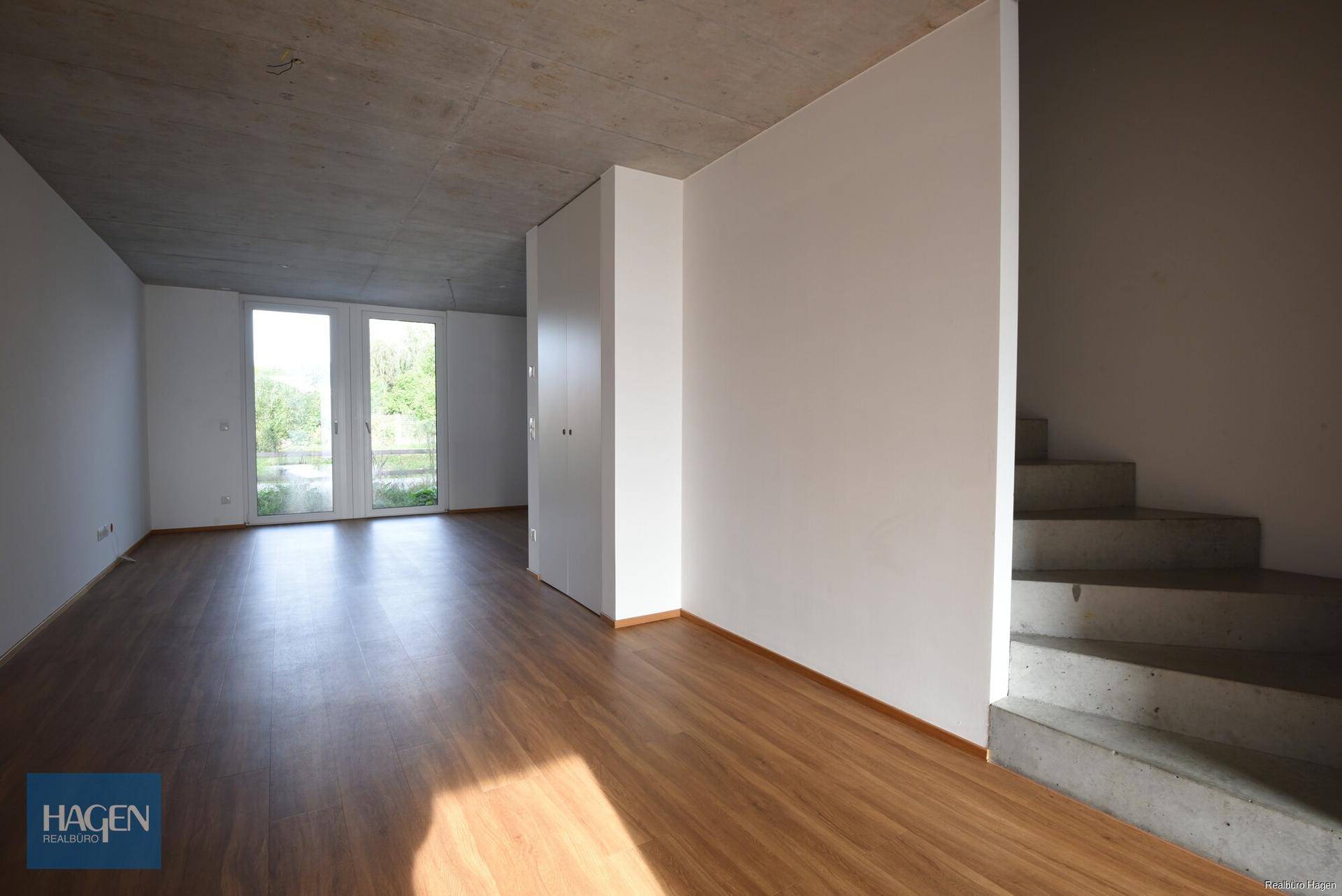Geräumiger, heller Raum mit Laminatboden, hohen Decken und Zugang zum Außenbereich.