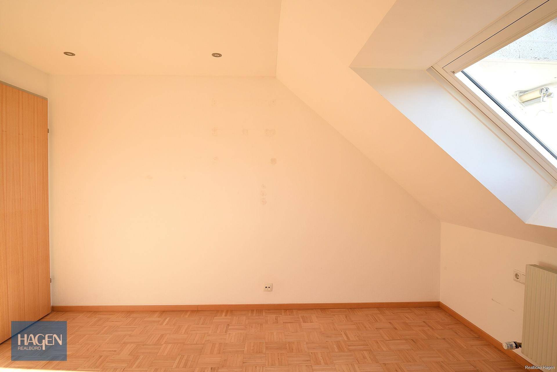 Helles Schlafzimmer im Dachgeschoss mit Parkettboden und Dachfenster in der Schräge.