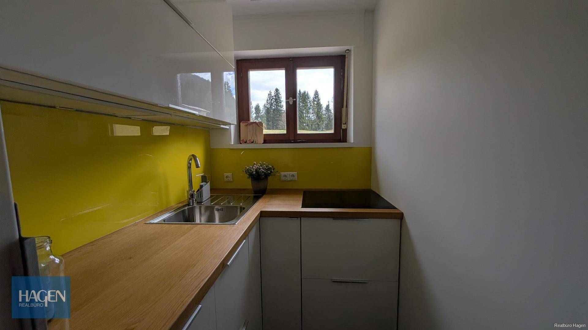 Moderne Küche mit gelber Rückwand, Holz-Arbeitsplatte und Fenster mit Blick ins Grüne.
