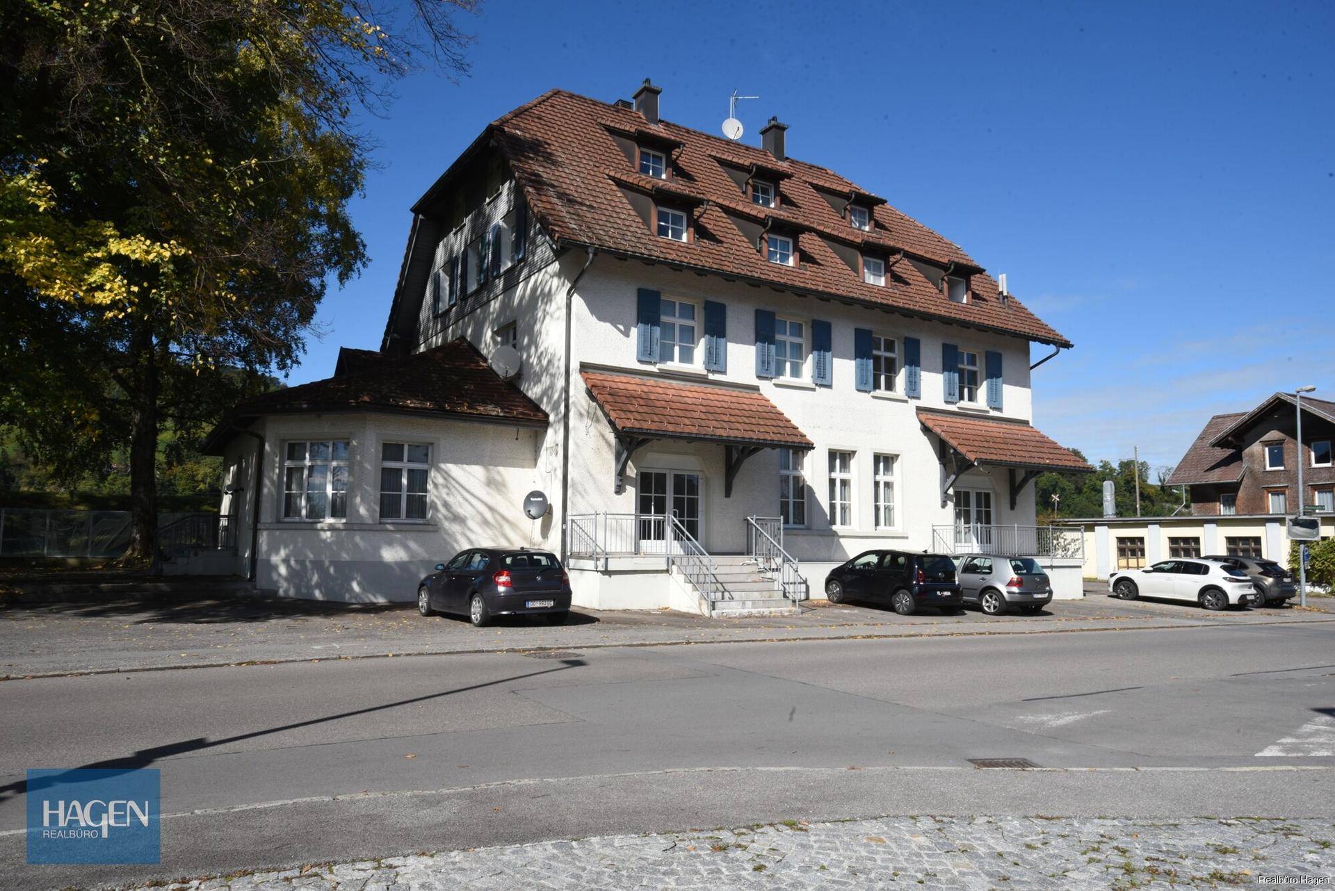 Klassisches Gebäude mit weißer Fassade, blauen Fensterläden und rotem Ziegeldach, gut erhalten.