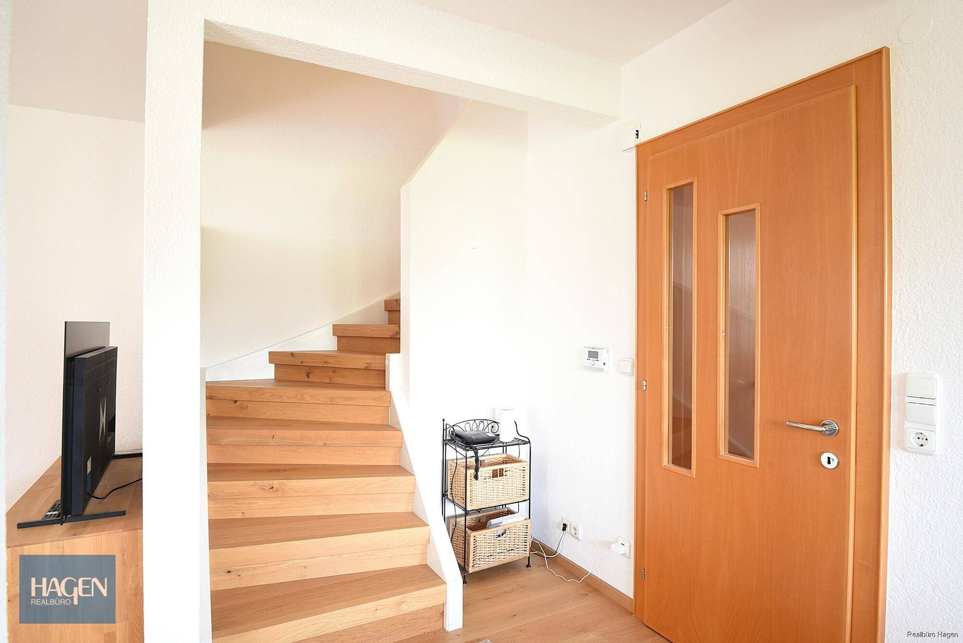 Heller Flur mit offener Holztreppe, die in die oberen Stockwerke des Hauses führt.