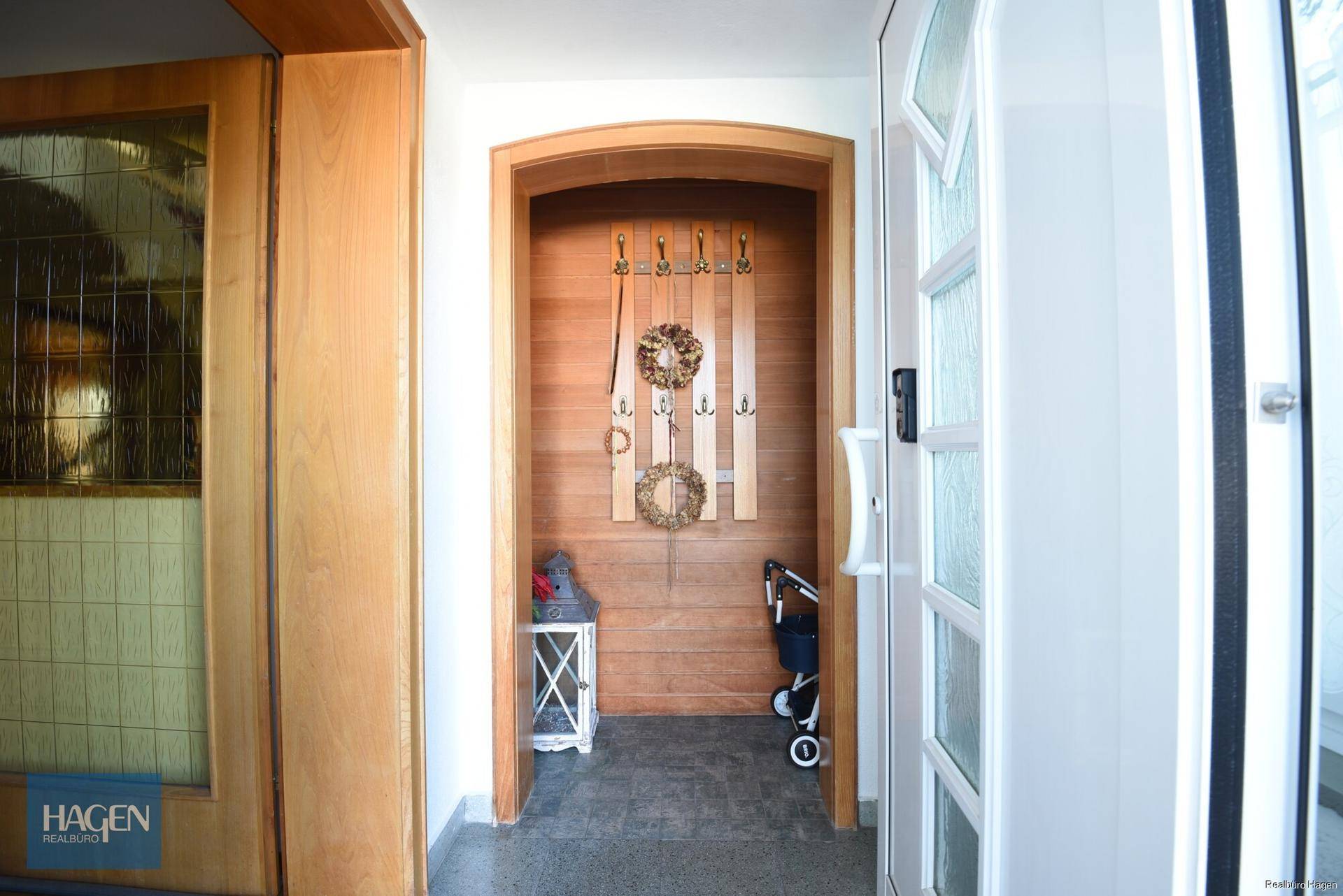 Heller Eingangsbereich mit Holztäfelung, Garderobe und dunklem Fliesenboden.
