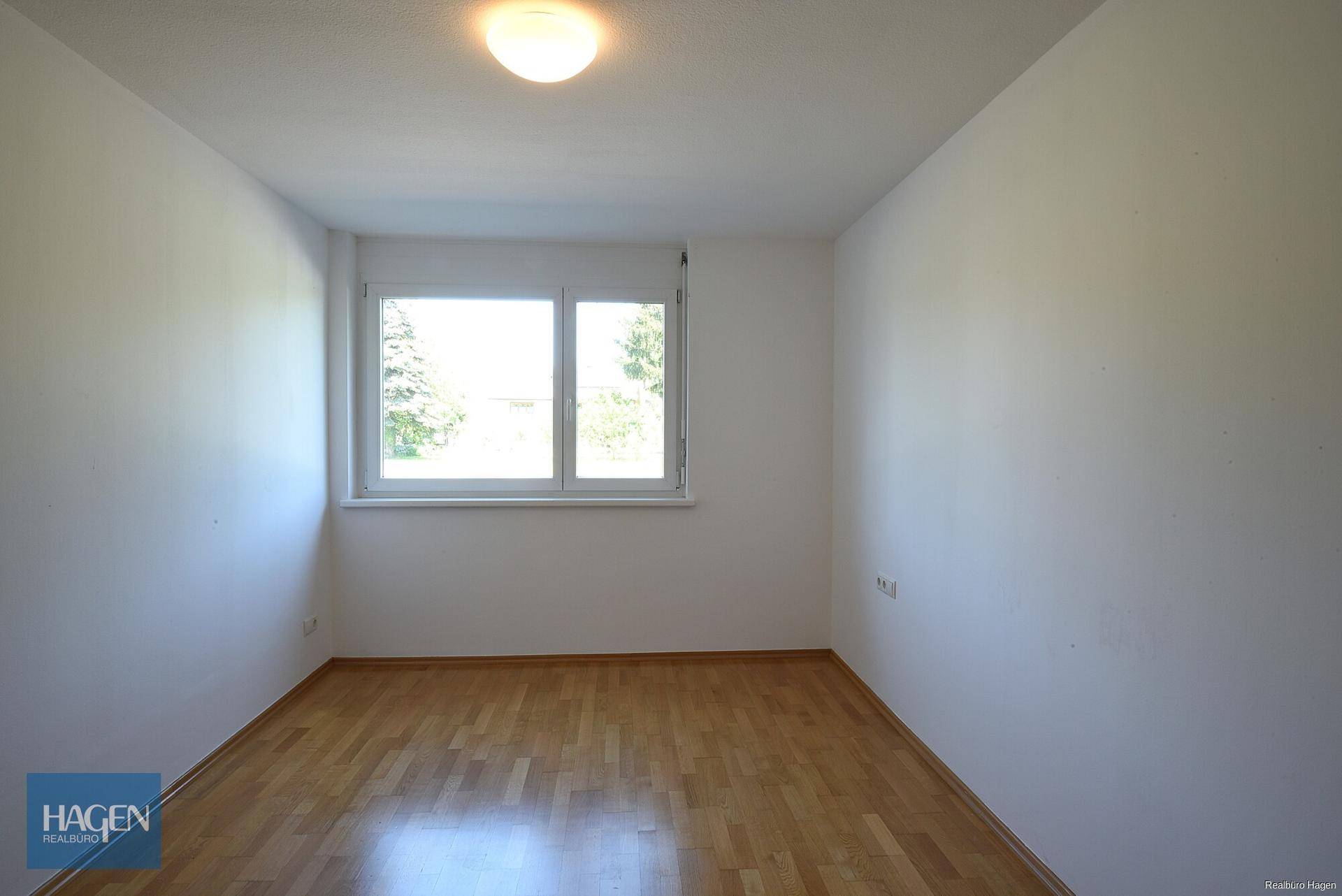 Freundliches Zimmer mit Parkettboden und großem Fenster für viel Tageslicht.