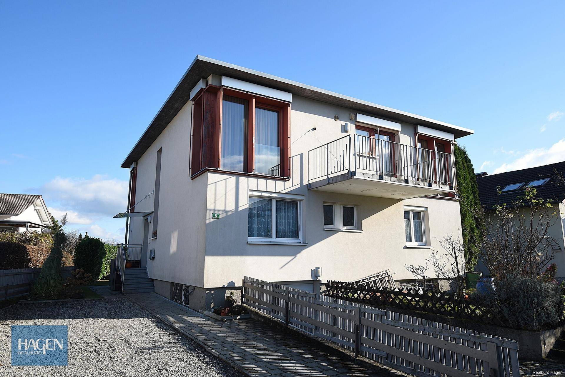 Seitenansicht des Hauses mit Balkon, Zufahrt und gepflegter Umgebung.