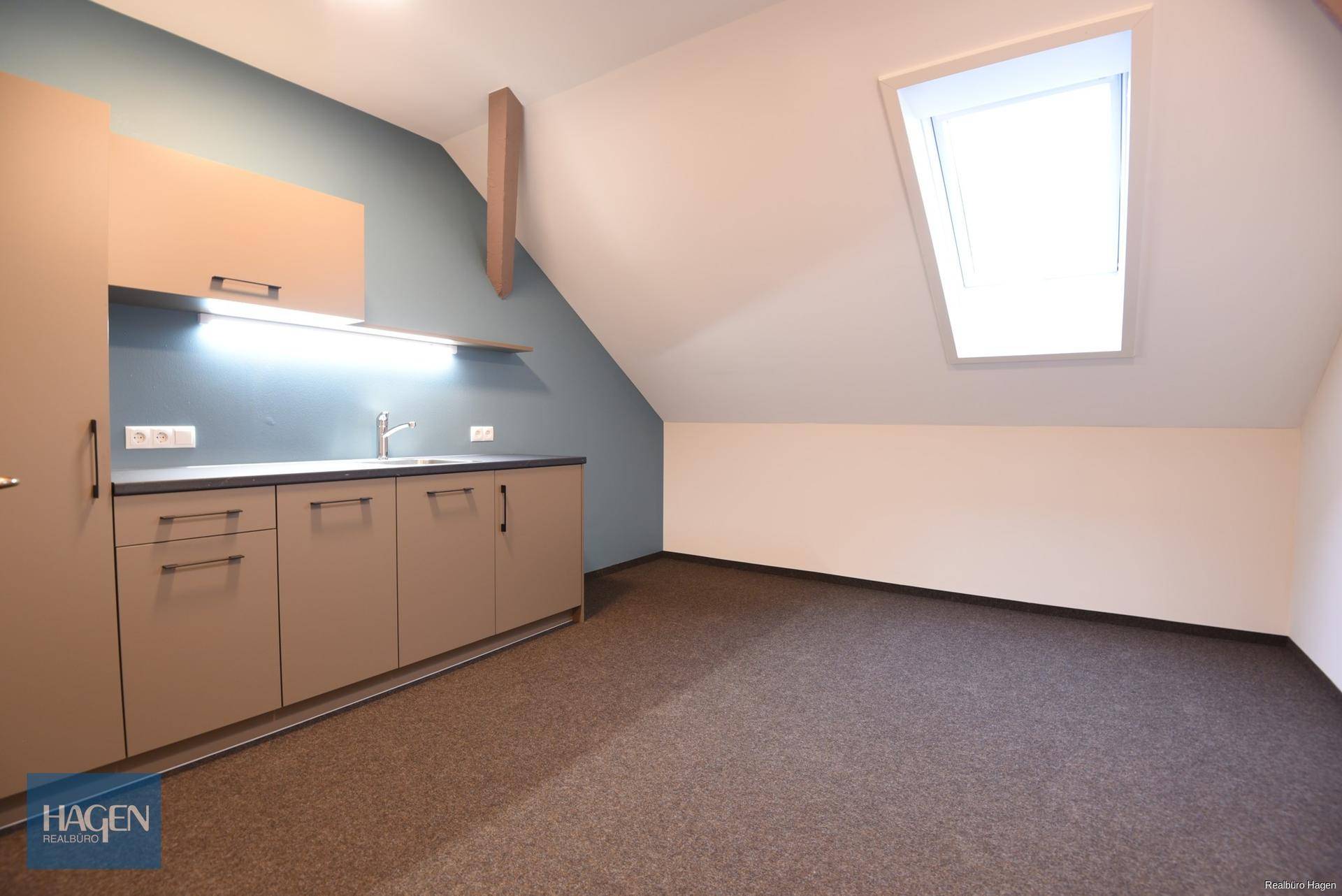 Heller Büroraum mit integrierter Teeküche, Dachschräge und einem Dachfenster für natürliches Licht.
