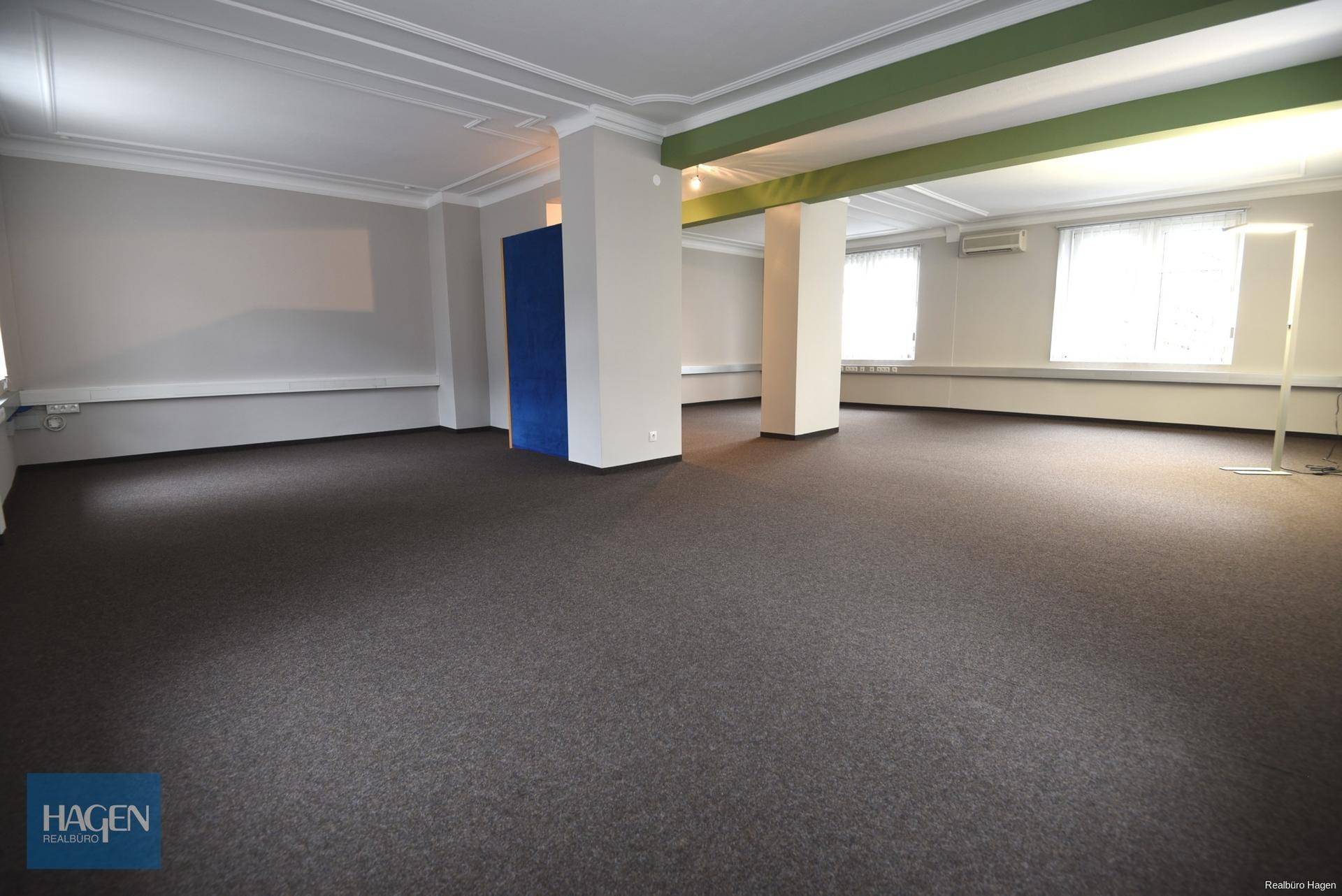 Weitläufiger Bürobereich mit Teppichboden, hohen Decken und großen Fenstern, bereit zur individuellen Gestaltung.