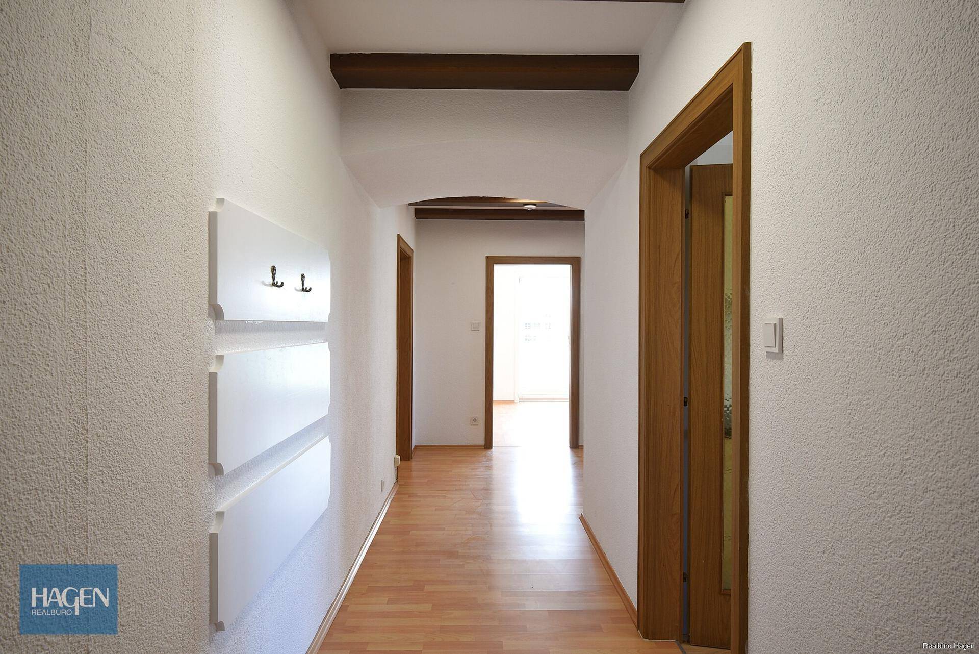 Langer Flur mit Laminatboden, Holztüren und sichtbaren Deckenbalken, der zu weiteren Räumen führt.