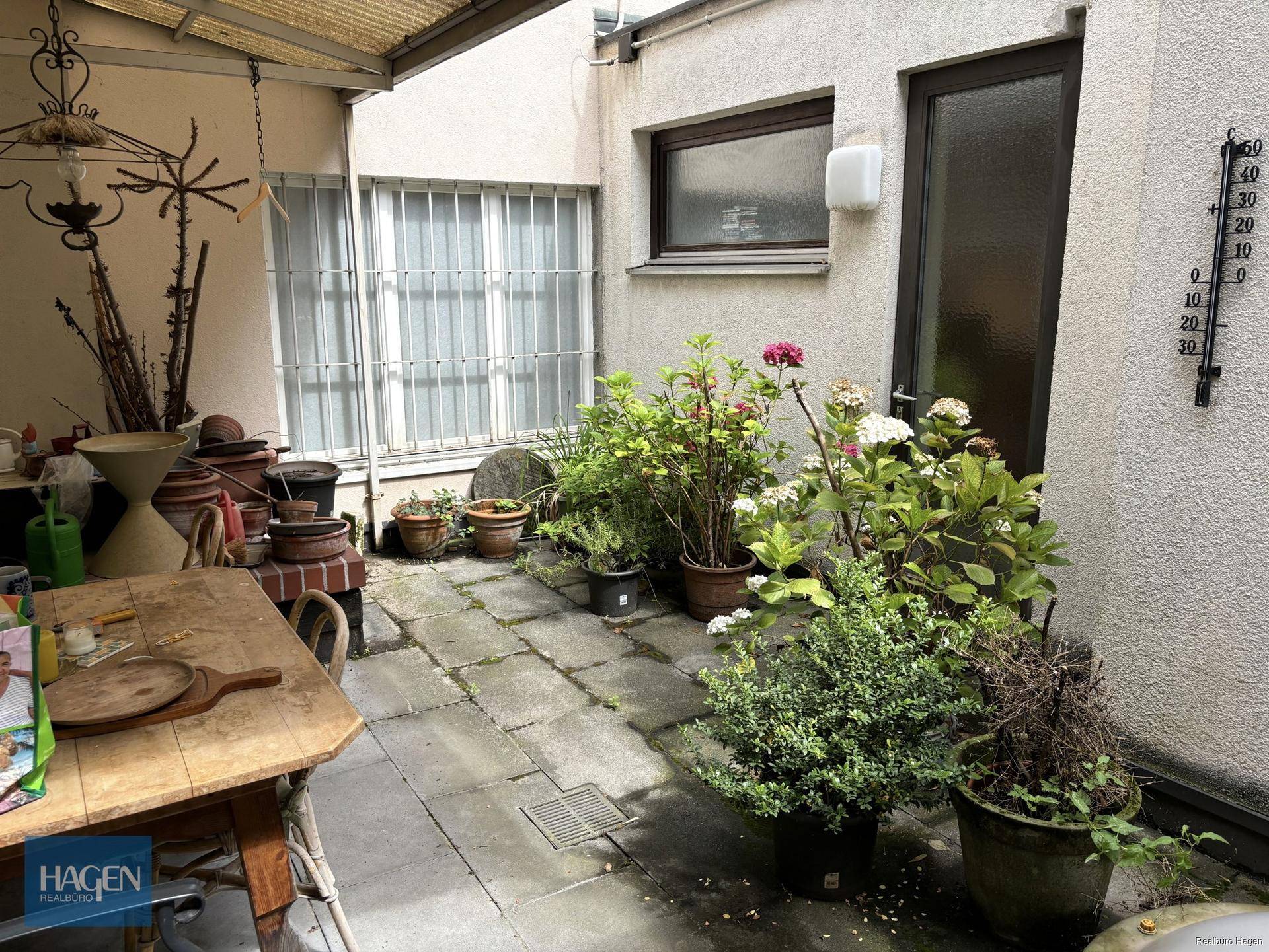 Gemütlicher Innenhof mit Pflanzen, Holztisch und Überdachung, ideal für Entspannung.
