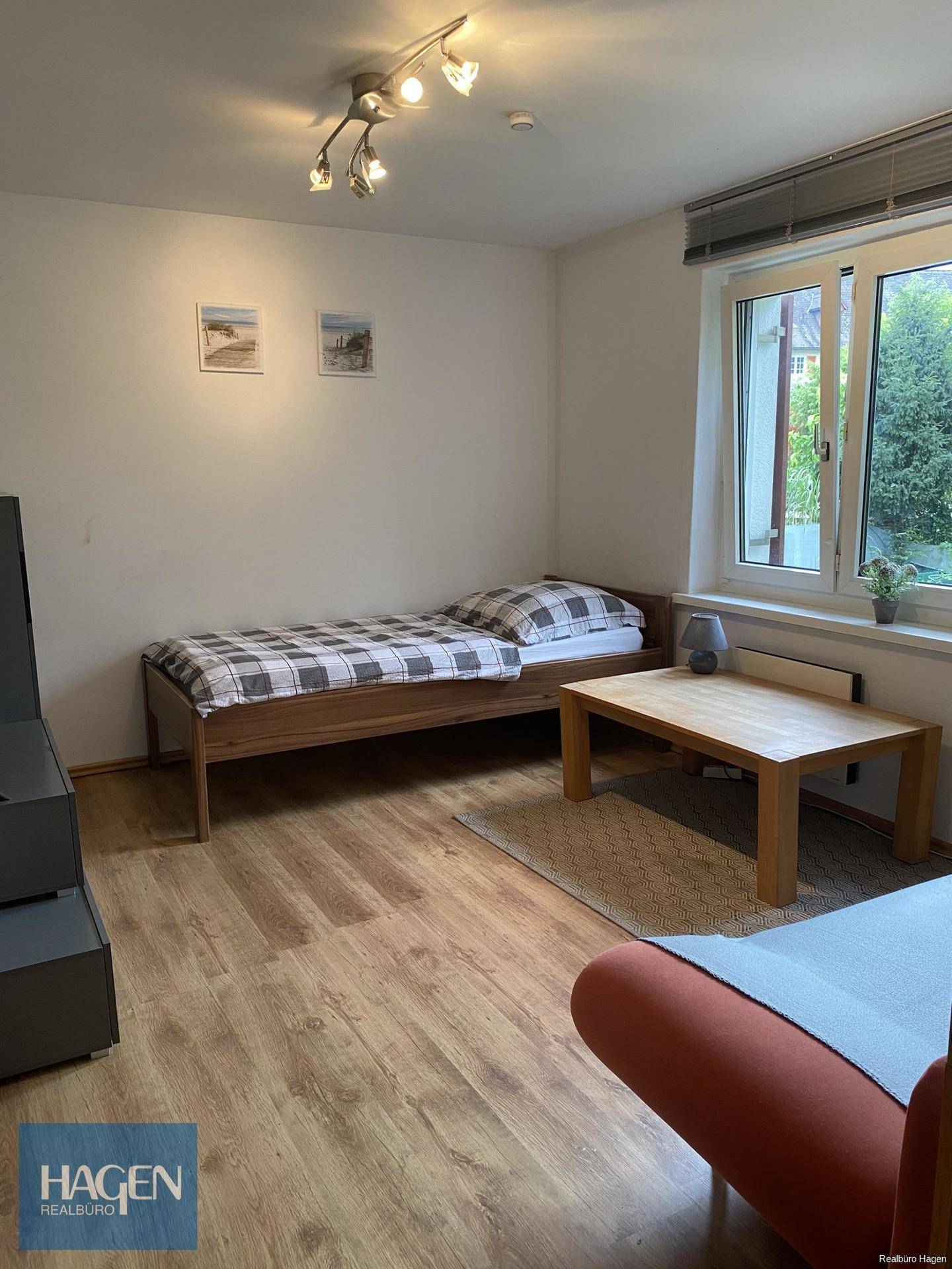 Helles Zimmer mit Einzelbett, Holzboden und einem großen Fenster mit Blick ins Grüne.