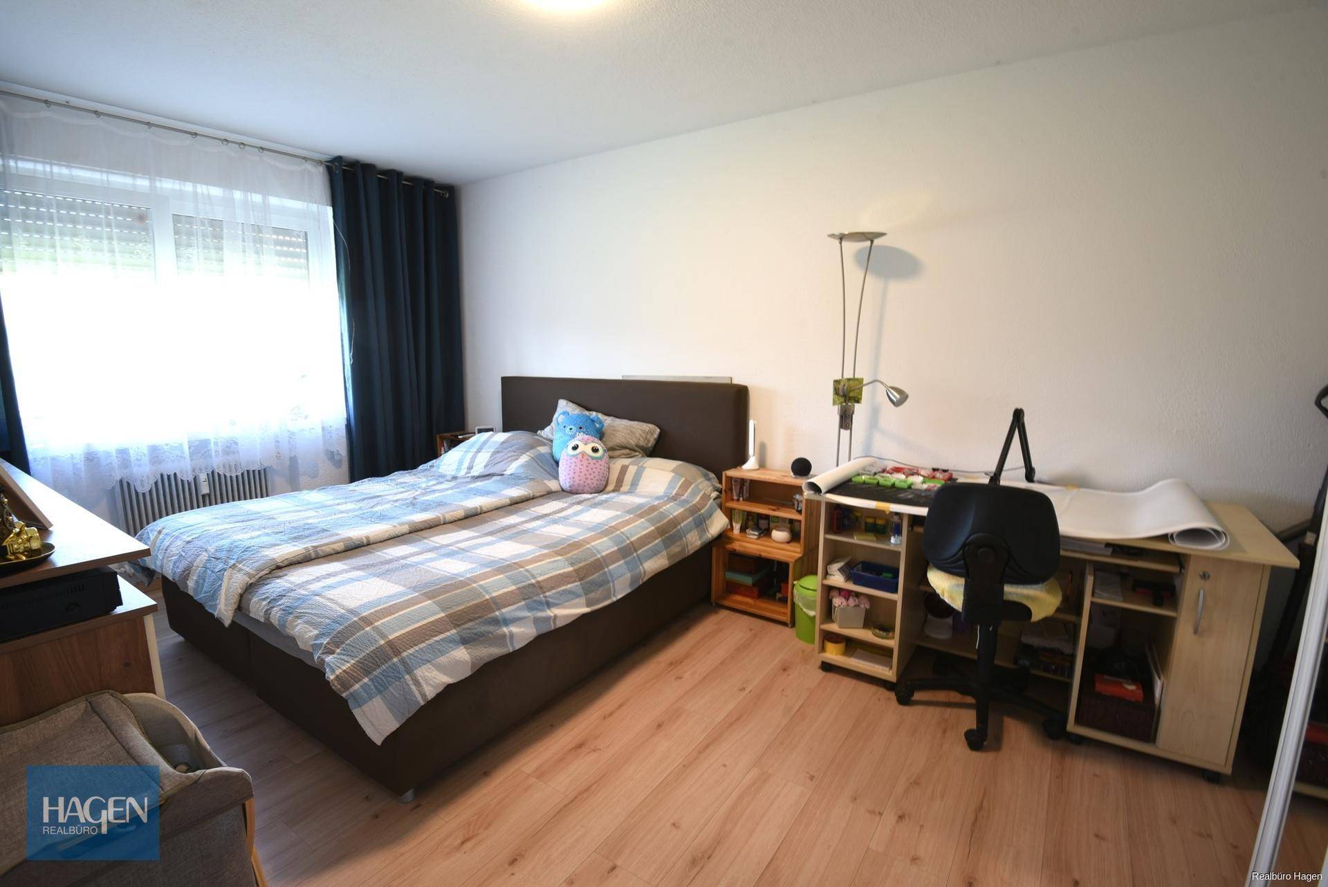 Schlafzimmer mit Doppelbett, Schreibtisch und Fenster, ausgestattet mit hellem Laminatboden.