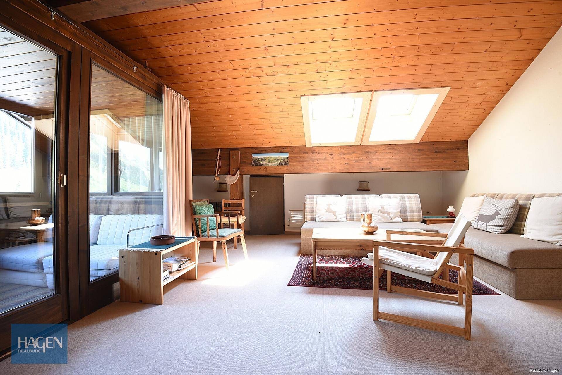 Gemütliches Wohnzimmer im alpinen Stil mit Holzbalkendecke, Dachfenstern und Zugang zu einem Wintergarten.