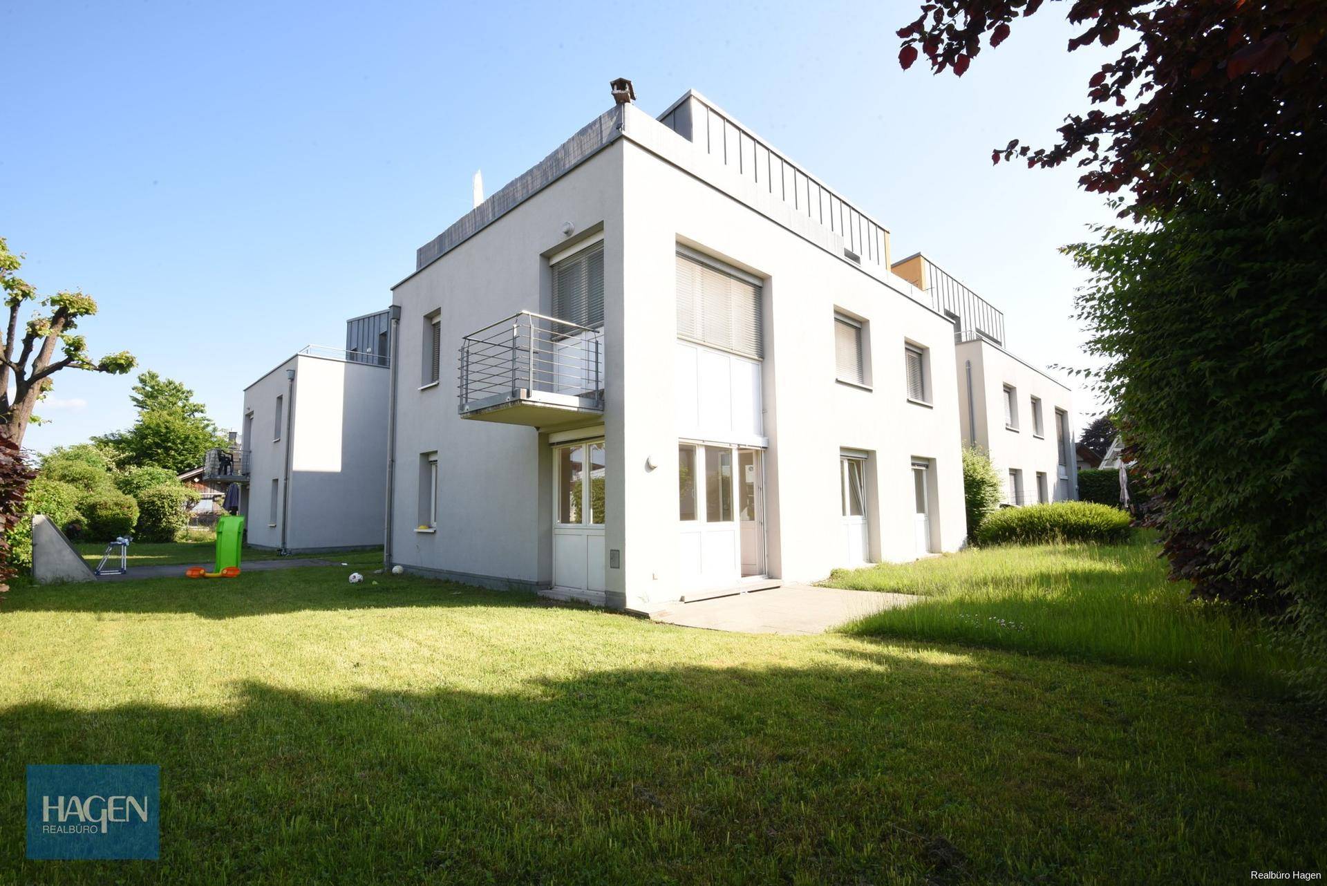 Moderne Wohnanlage mit weißer Fassade und gepflegtem Rasen im Sommerlicht.