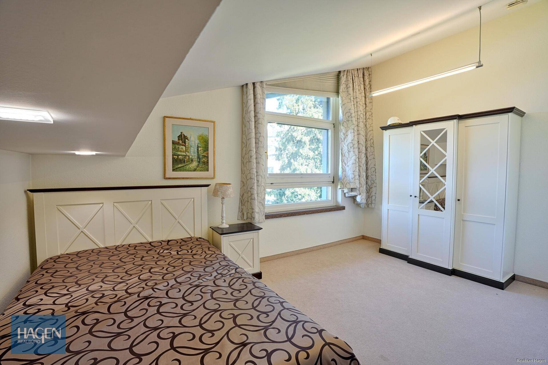 Gemütliches Schlafzimmer im Dachgeschoss mit Teppichboden, großem Fenster und Kleiderschrank.
