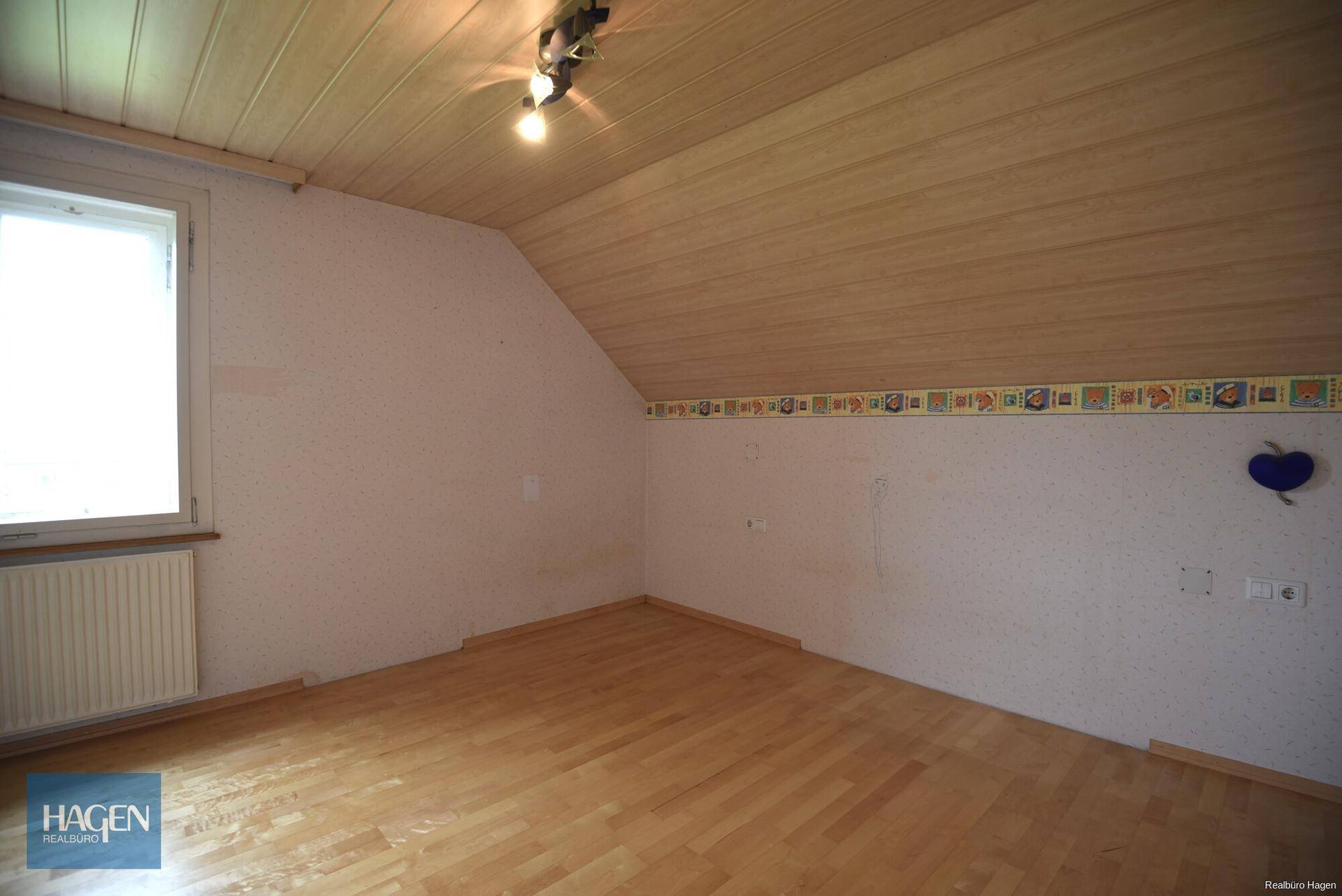 Dachgeschoss-Schlafzimmer mit schräger Decke, Holzboden und Fenster.