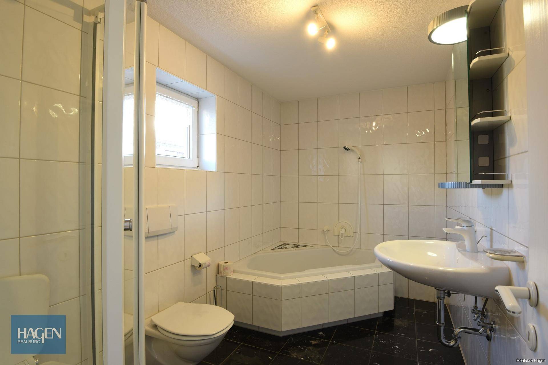 Badezimmer mit Eckbadewanne, Dusche, WC und Waschbecken, hell gefliest und mit Fenster.