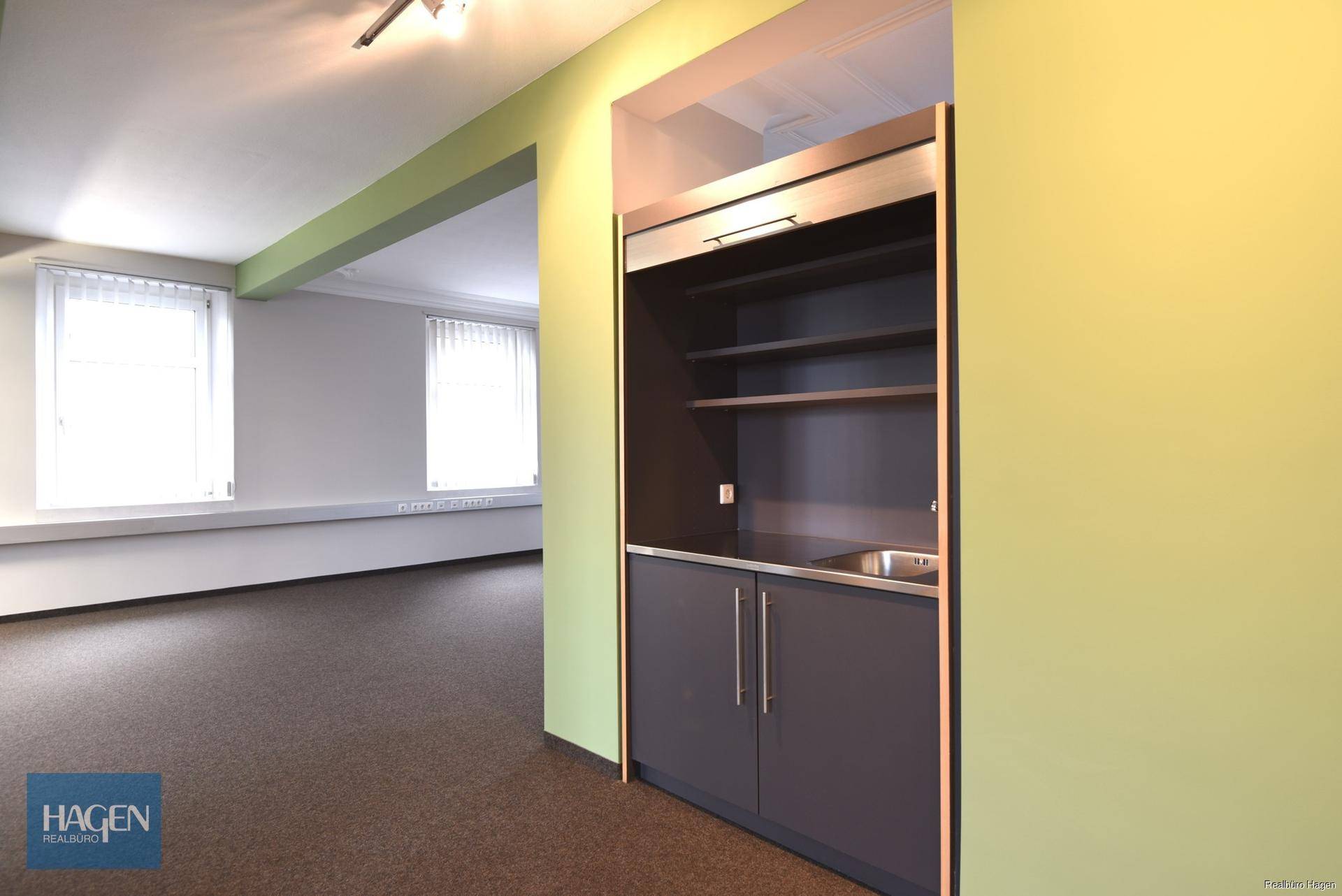 Kleine, funktionale Teeküche mit Spülbecken und Stauraum, integriert in einen Bürobereich.