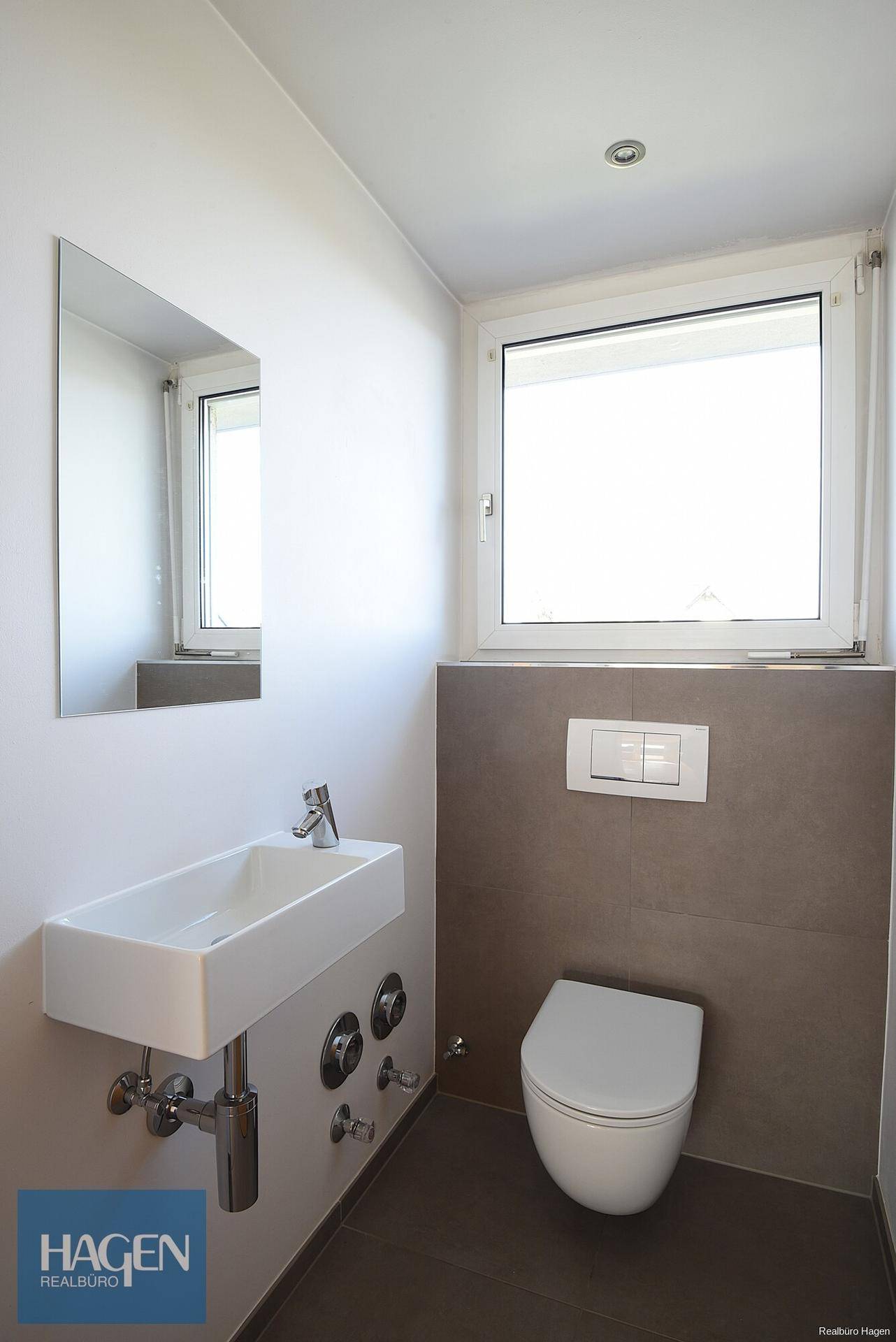 Modernes Gäste-WC mit wandhängendem WC, kleinem Waschbecken und Fenster für Tageslicht.