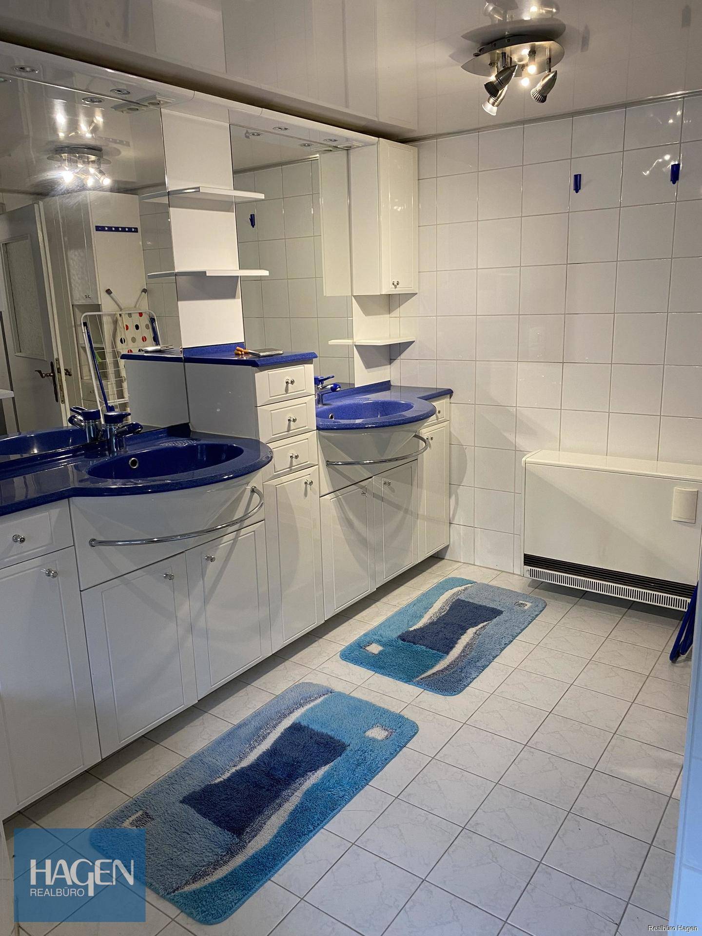 Badezimmer mit Doppelwaschbecken, blauen Akzenten und einem hellen Fliesenboden.