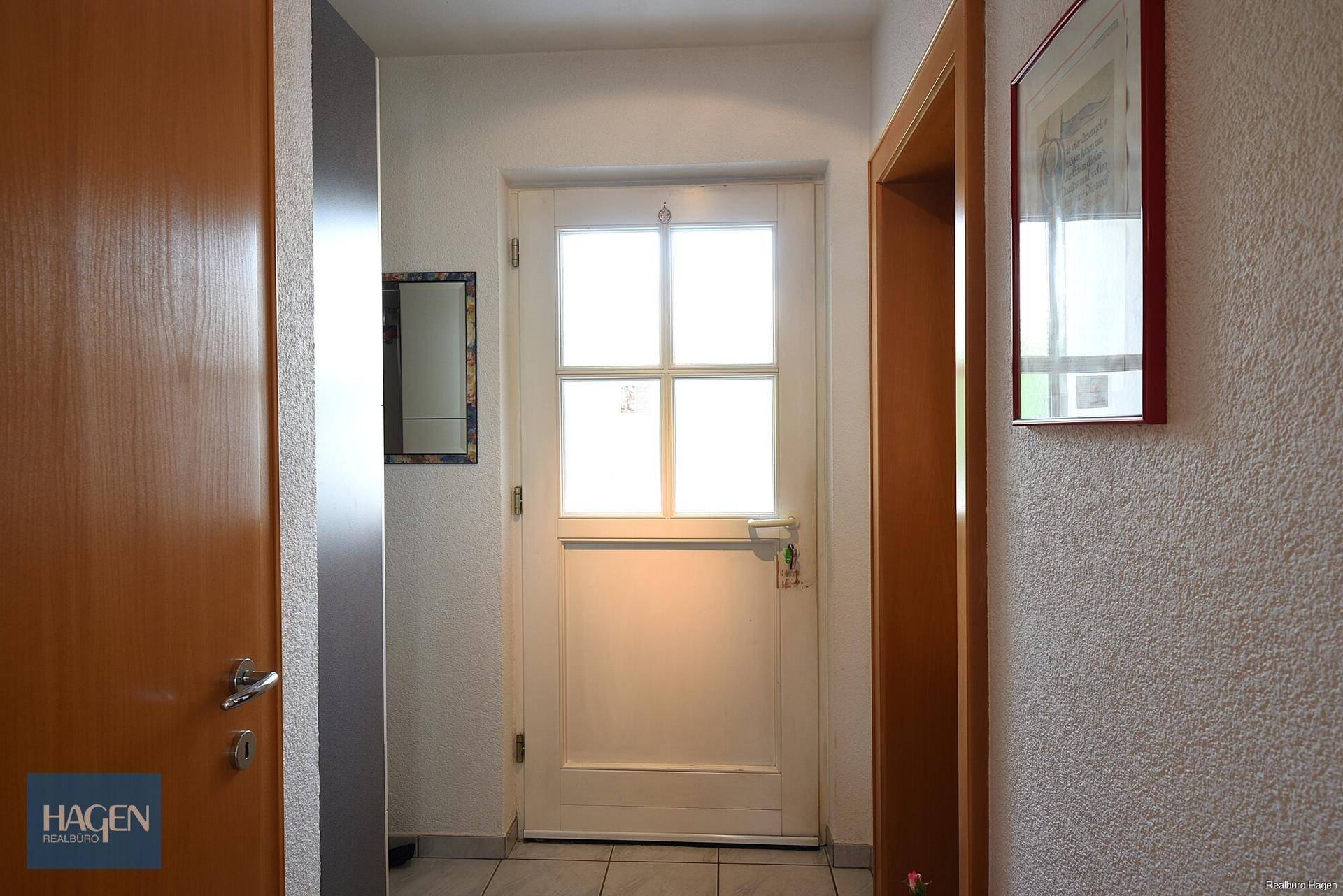 Eingangsbereich mit weißer Haustür, Fliesenboden und ausreichend Platz für Garderobe.