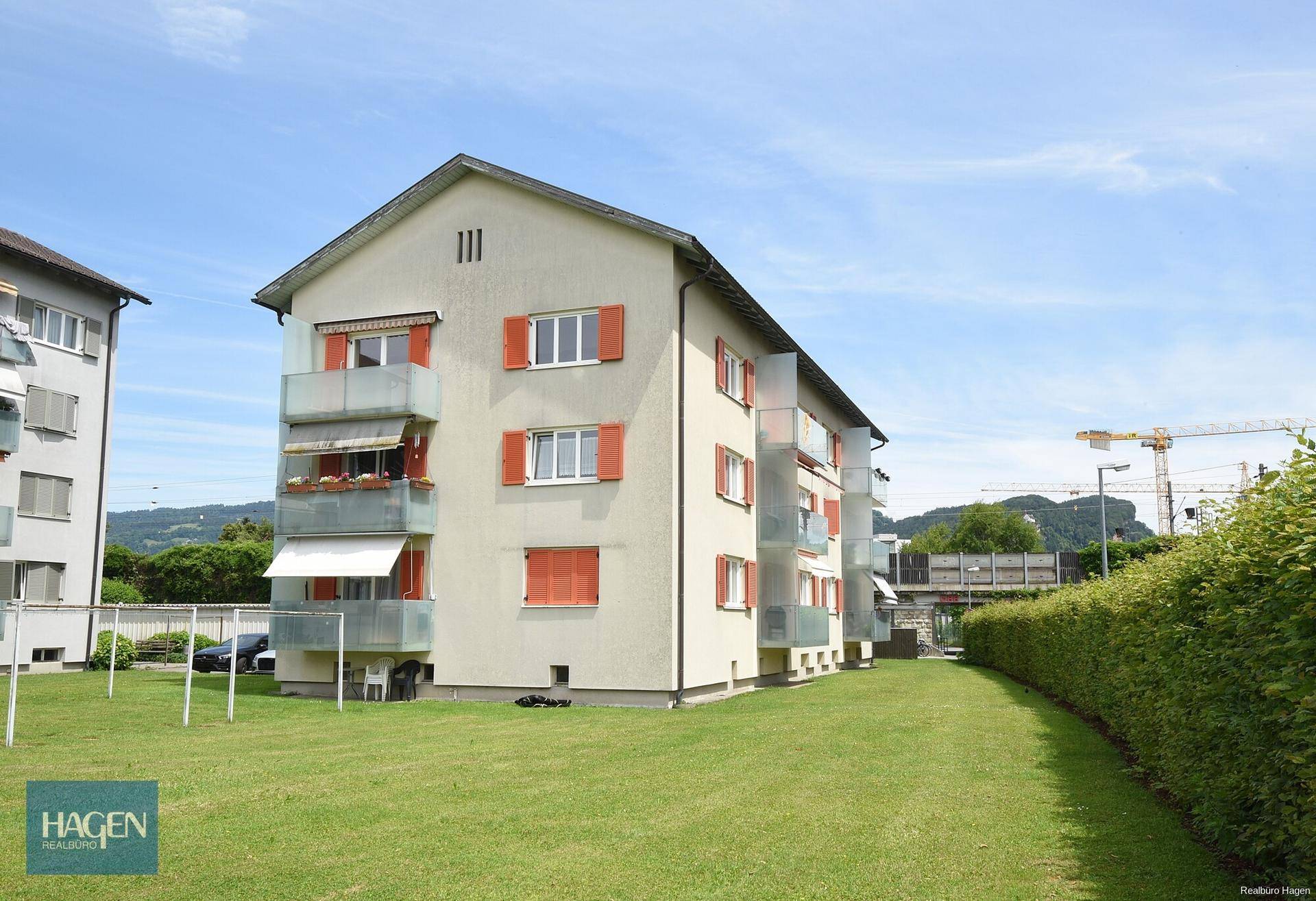Mehrfamilienhaus mit gepflegter Rasenfläche und Balkonen in sonniger Lage, umgeben von Grün.