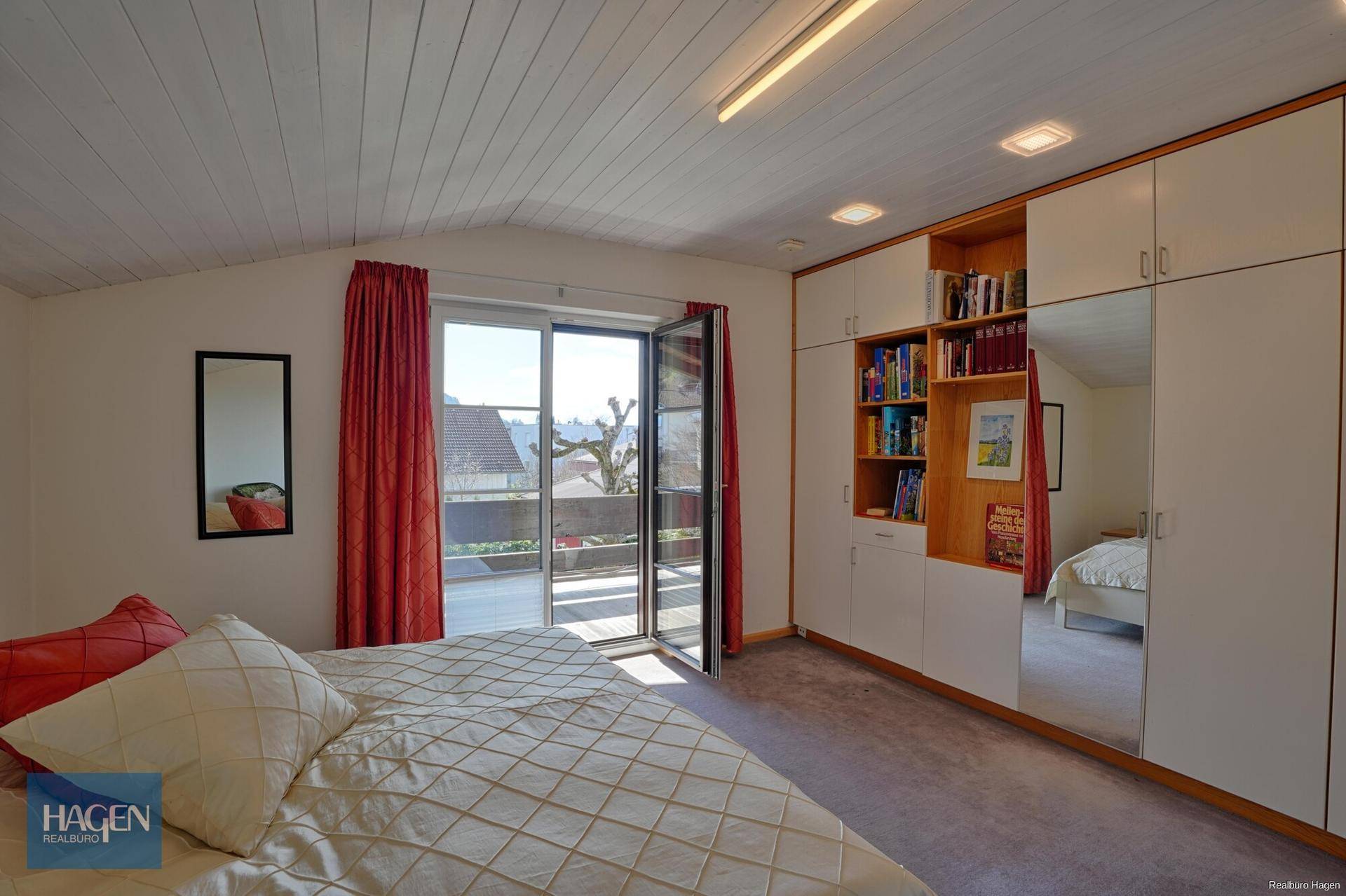 Schlafzimmer mit Einbauschränken, Holzdecke und Zugang zu einem großen Balkon.