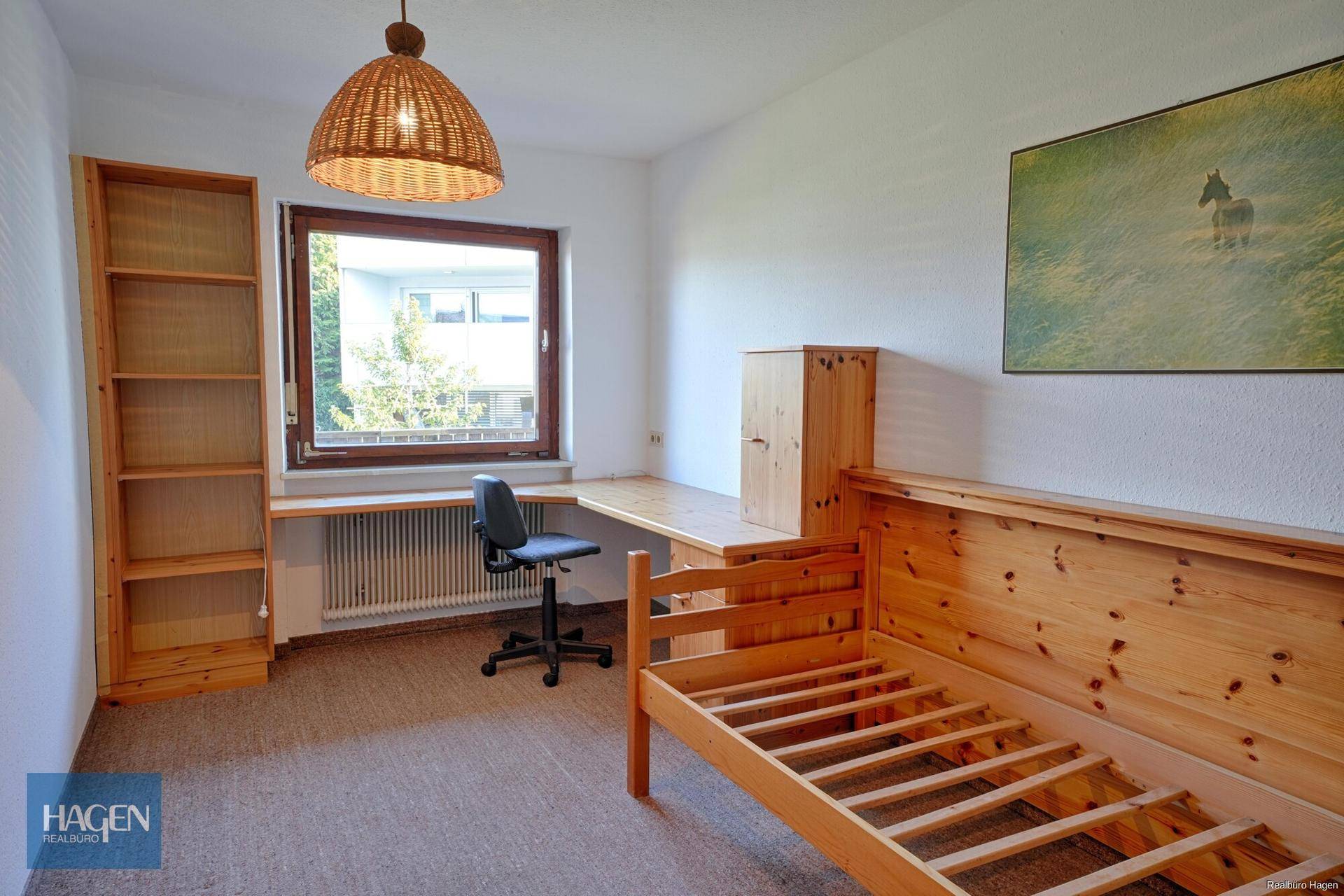 Schlafzimmer mit Holzbett, Schreibtisch und Regal, hell durch großes Fenster.
