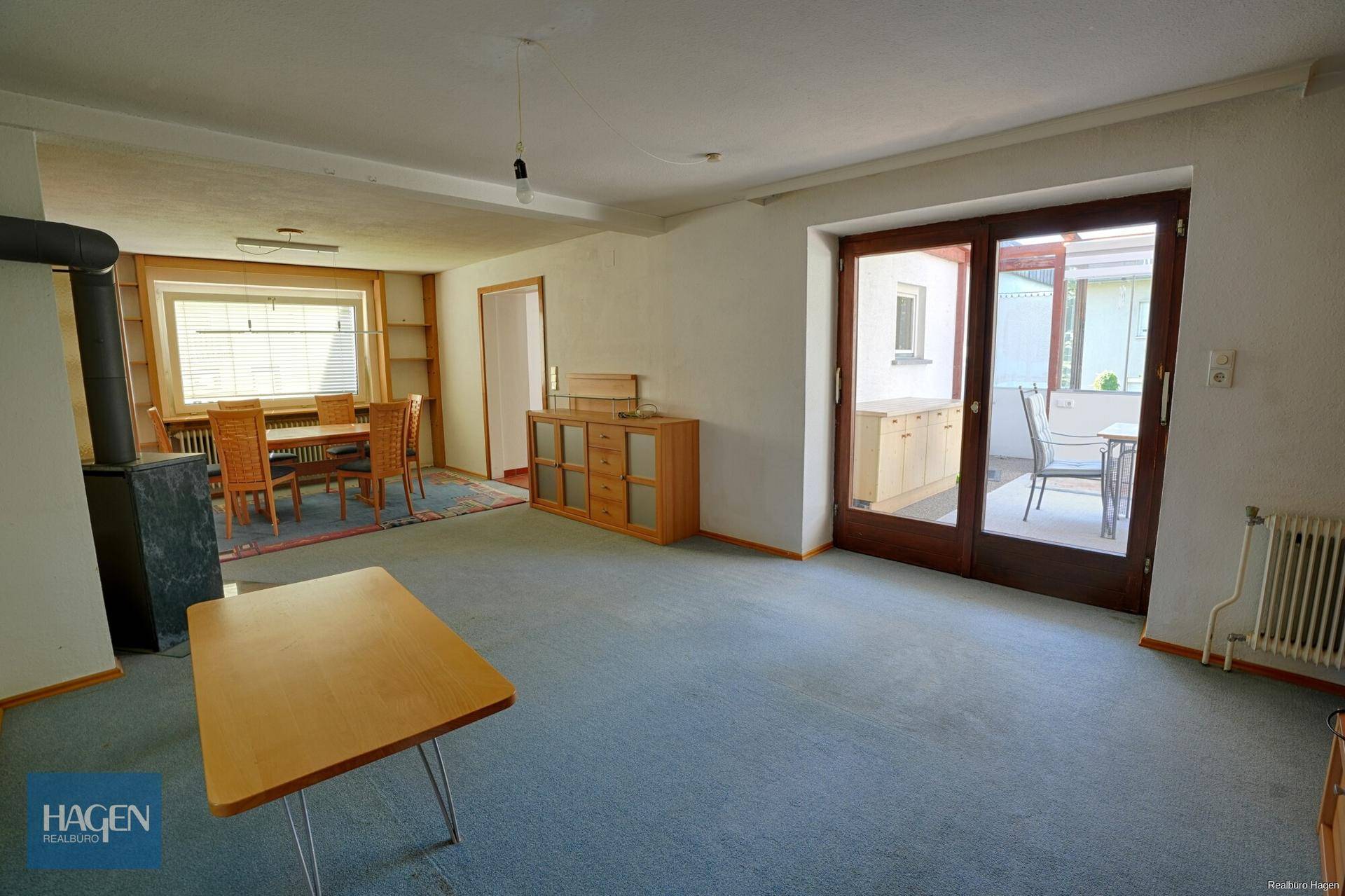 Geräumiger Wohn- und Essbereich mit Teppichboden, Kaminofen und Zugang zur Terrasse.