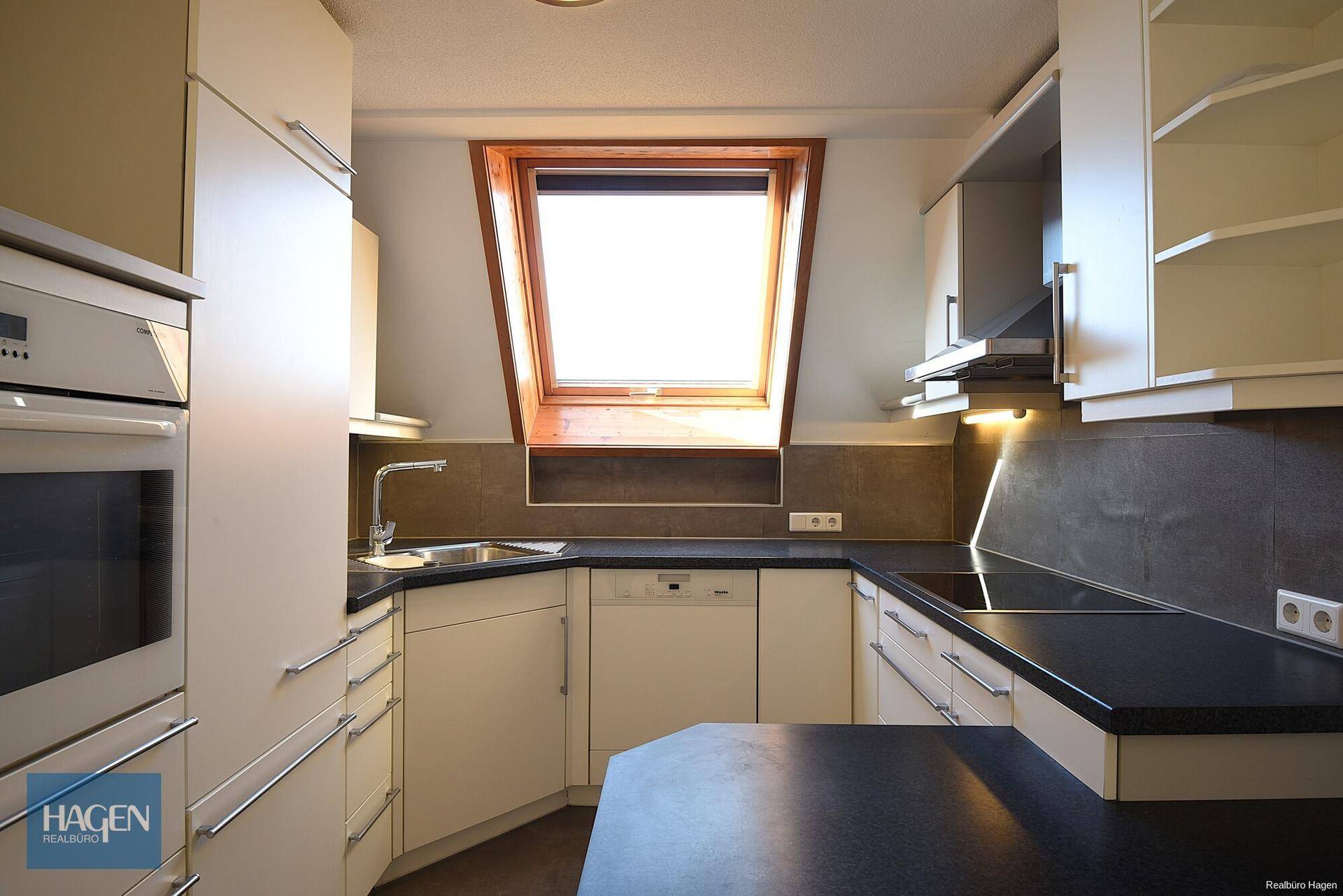 Moderne Einbauküche mit weißen Schränken, dunklen Arbeitsplatten und Dachfenster für viel Licht.