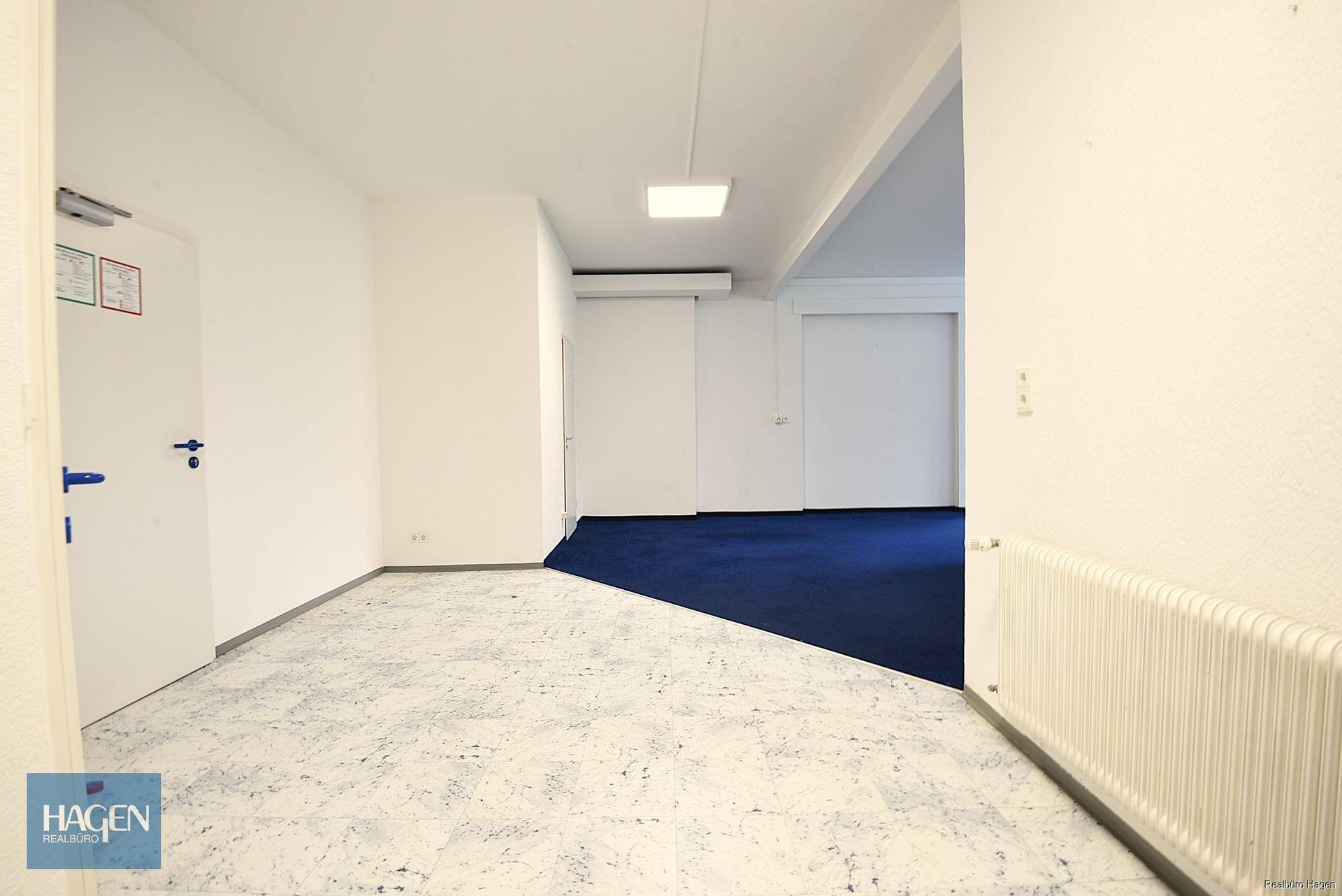 Langer Flur mit Fliesenboden auf der einen Seite und blauem Teppichboden auf der anderen Seite.