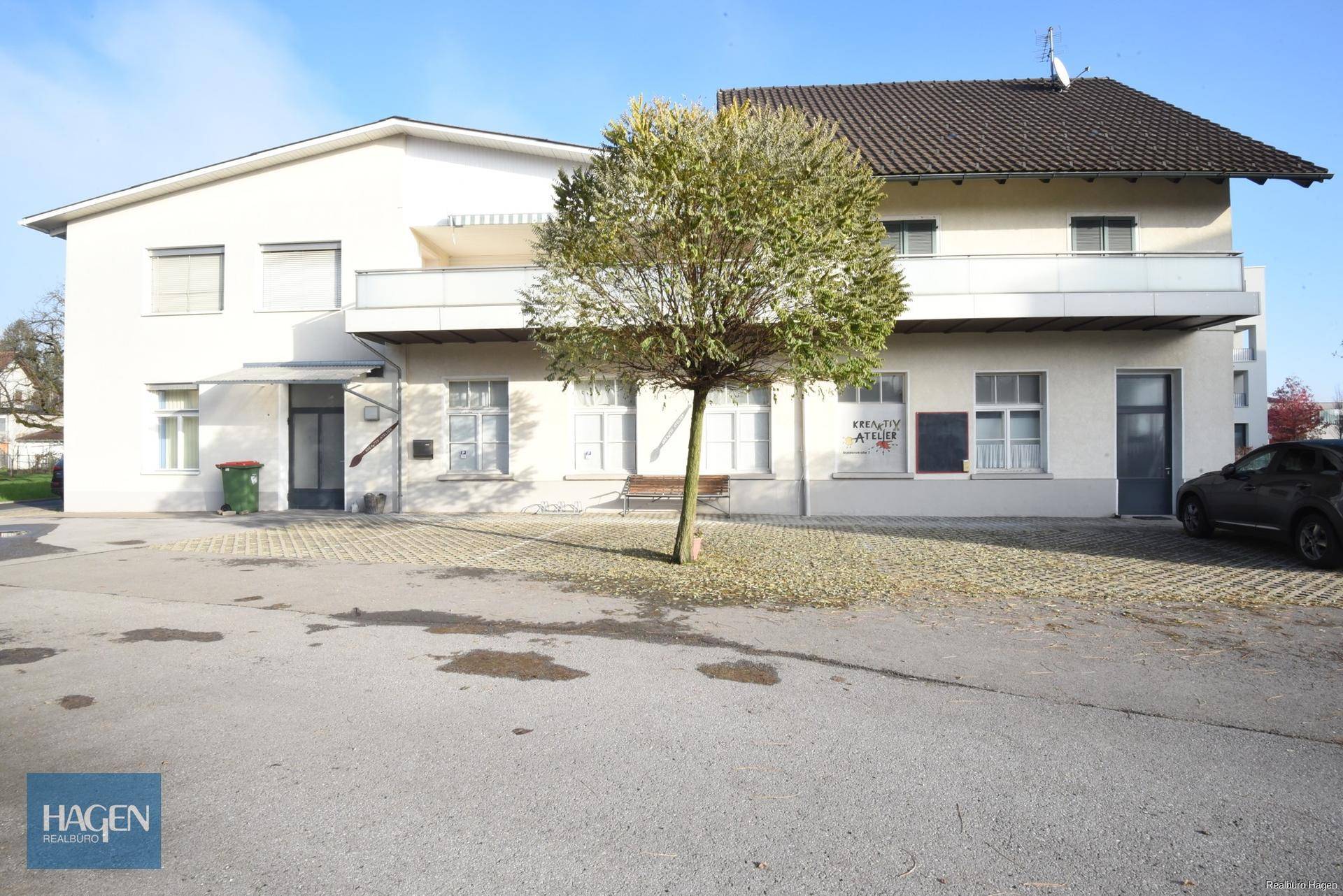 Rückansicht des Gebäudes mit einem Baum im Vordergrund und einem großen Parkplatzbereich.
