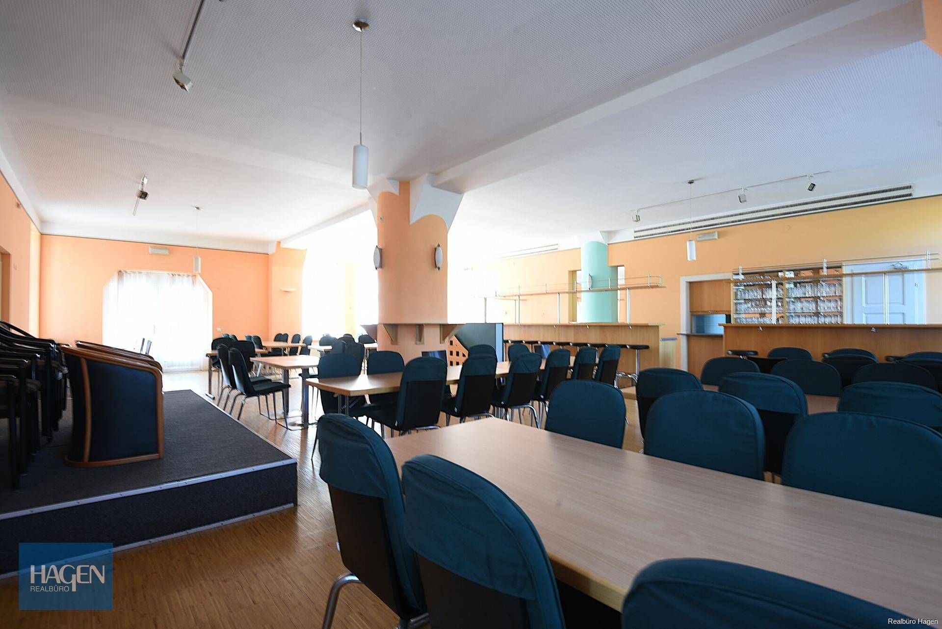 Geräumiger Saal mit vielen Tischen und Stühlen, ideal für Versammlungen oder Gastronomiebetriebe.