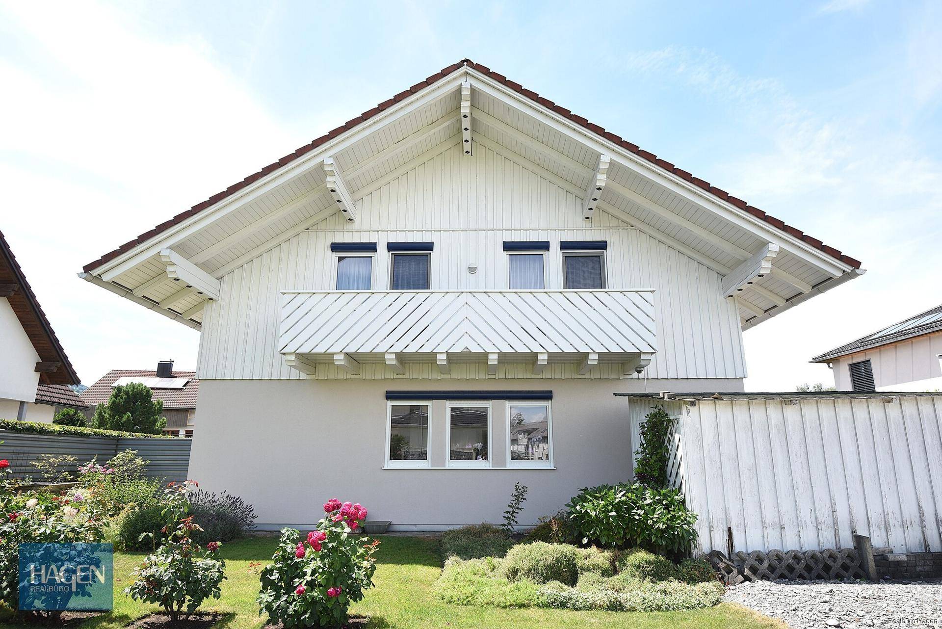 Frontansicht des Einfamilienhauses mit Balkon, gepflegtem Vorgarten und traditioneller Fassade.