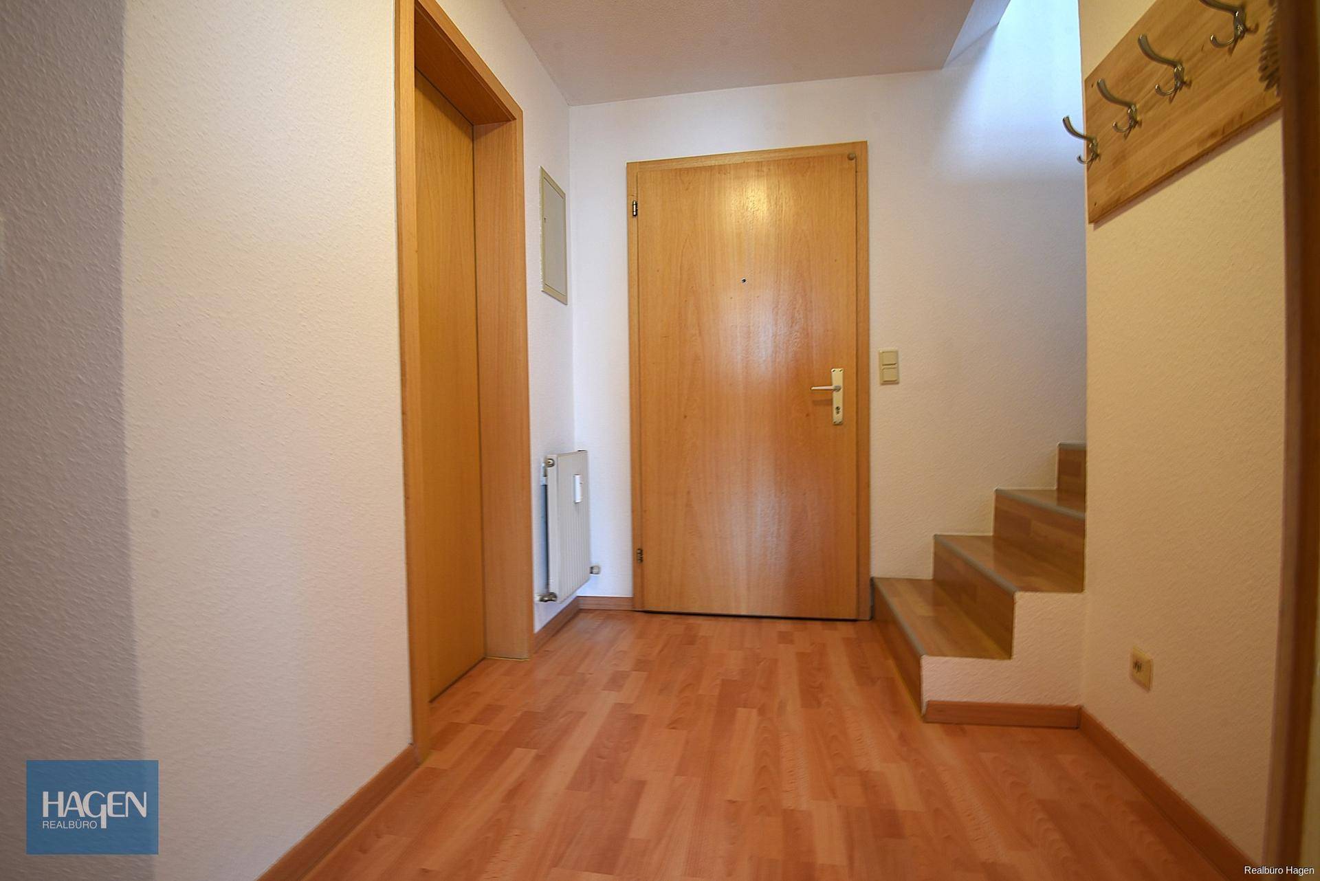 Eingangsbereich mit Garderobe, Holztür und Treppe zum Obergeschoss.