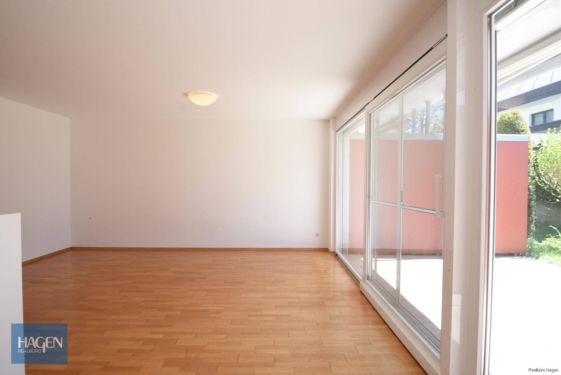 Geräumiges Wohnzimmer mit hellem Parkettboden und breiter Fensterfront zum Außenbereich.