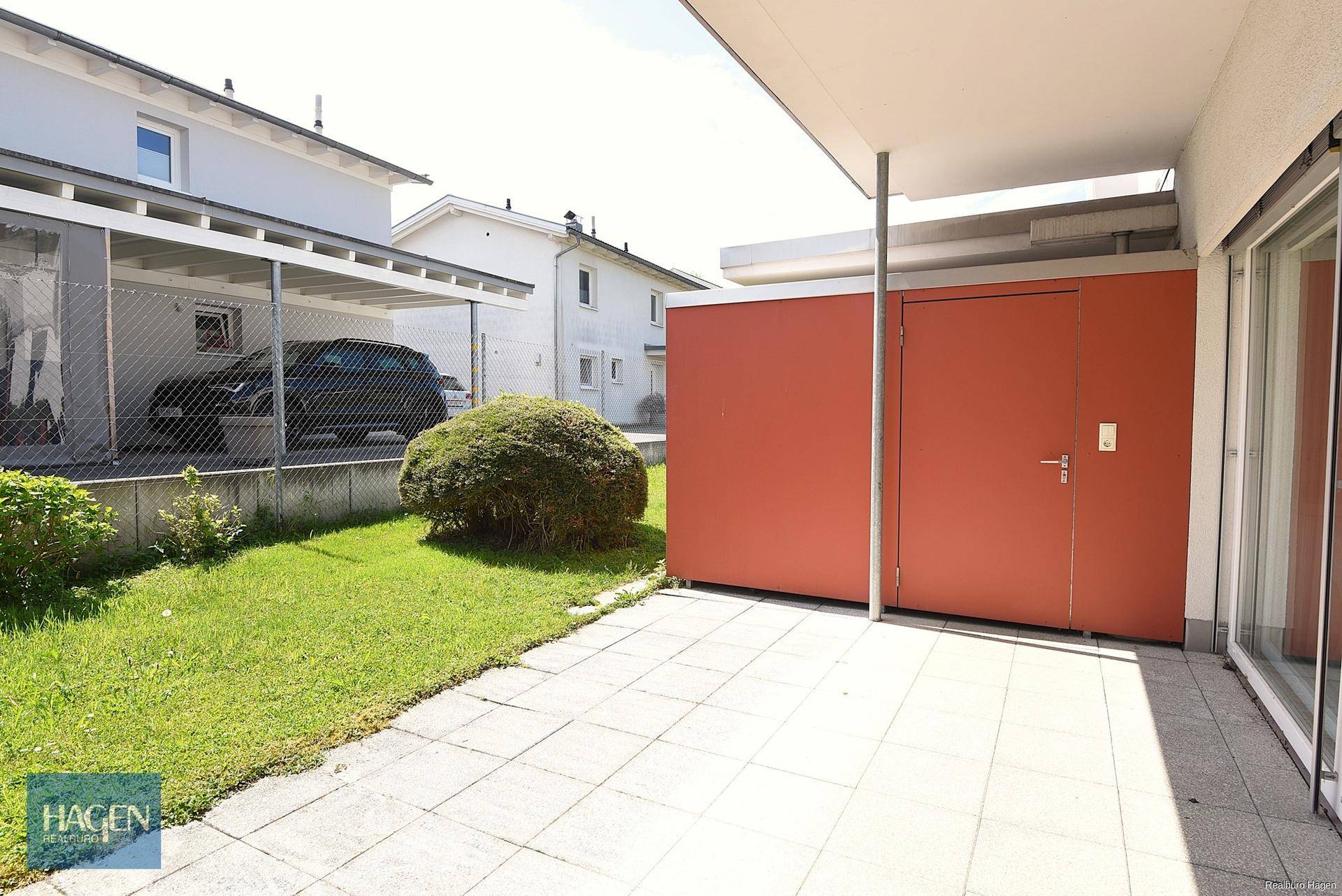Gepflasterte Terrasse mit rotem Abstellraum und Zugang zu einem kleinen Rasenbereich.