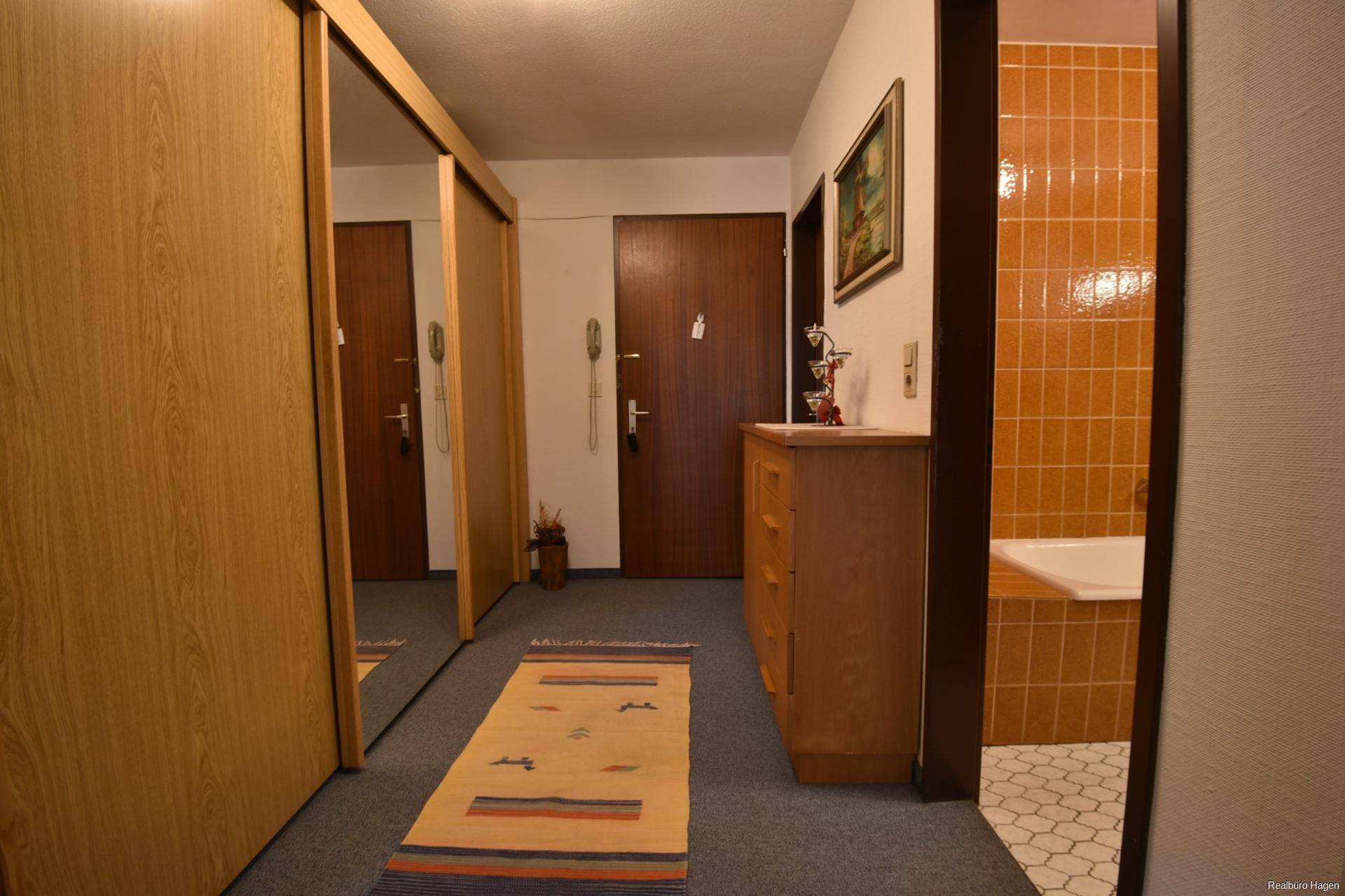 Flur mit Spiegelschränken, einer Kommode und Blick in ein Badezimmer mit orangefarbenen Fliesen.
