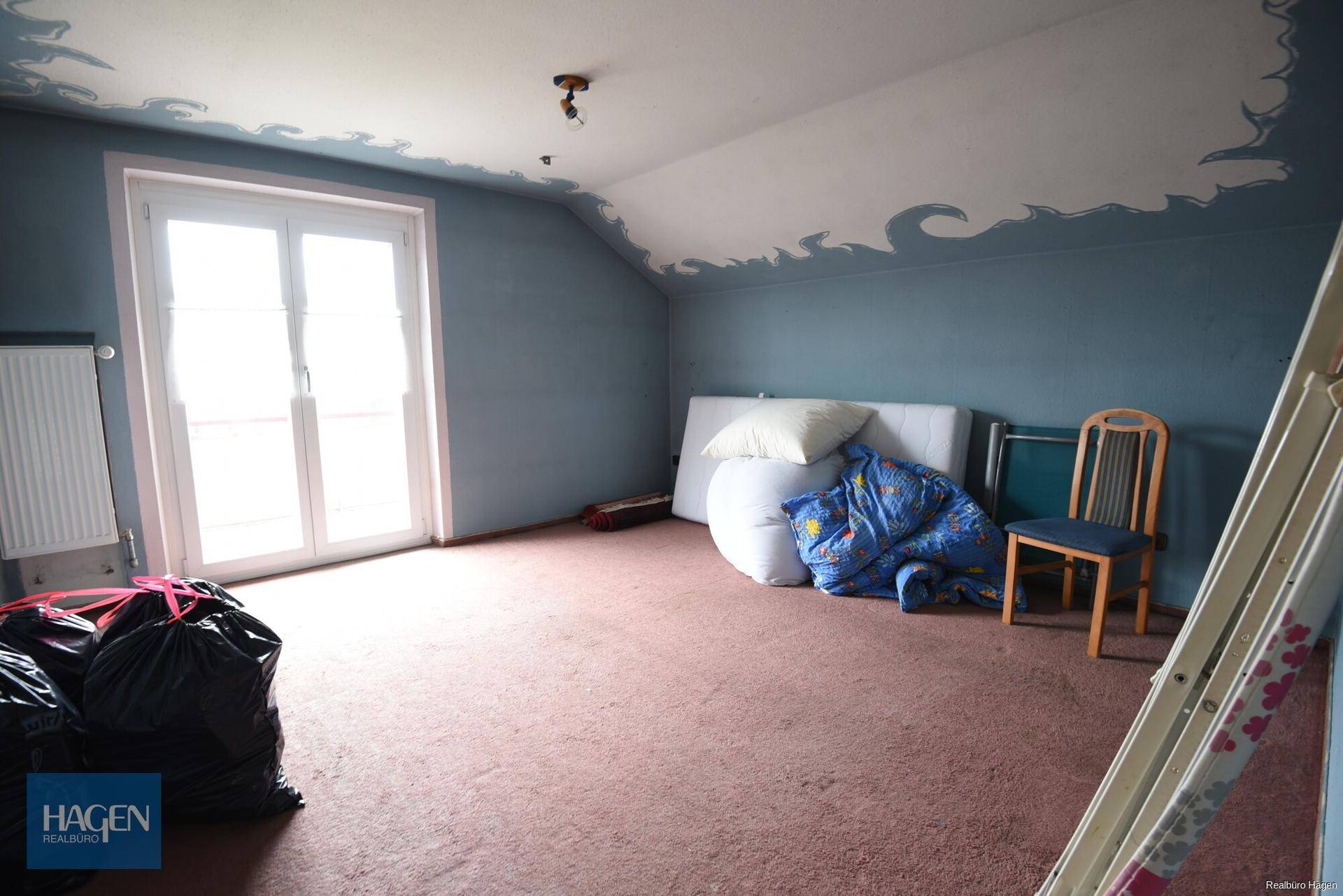 Dachgeschosszimmer mit blauen Wänden, Teppichboden und Zugang zum Balkon.