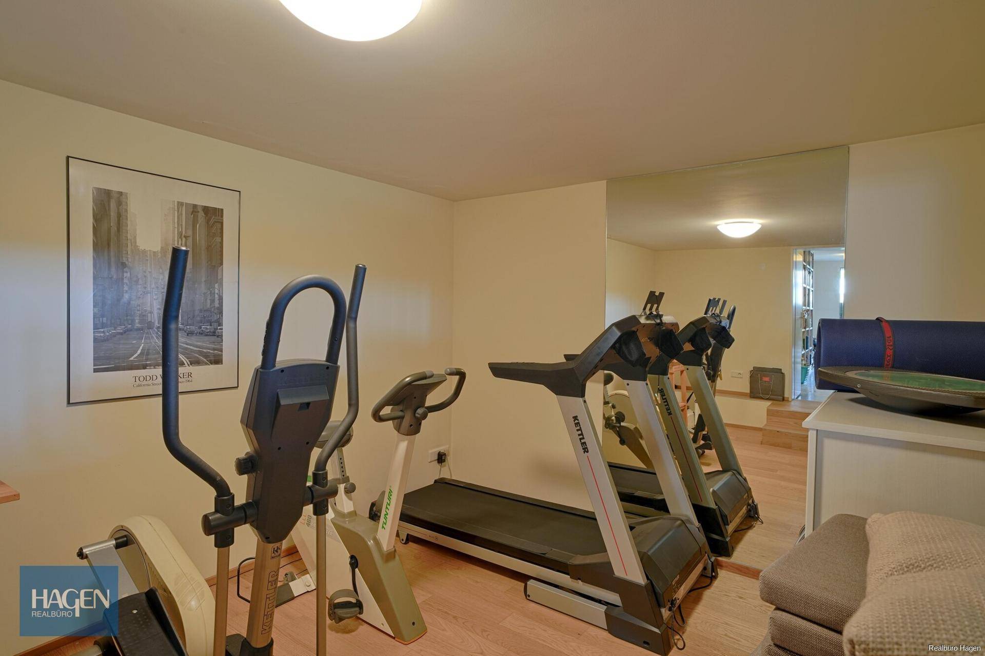 Fitnessraum im Untergeschoss mit verschiedenen Trainingsgeräten und Spiegelfläche.